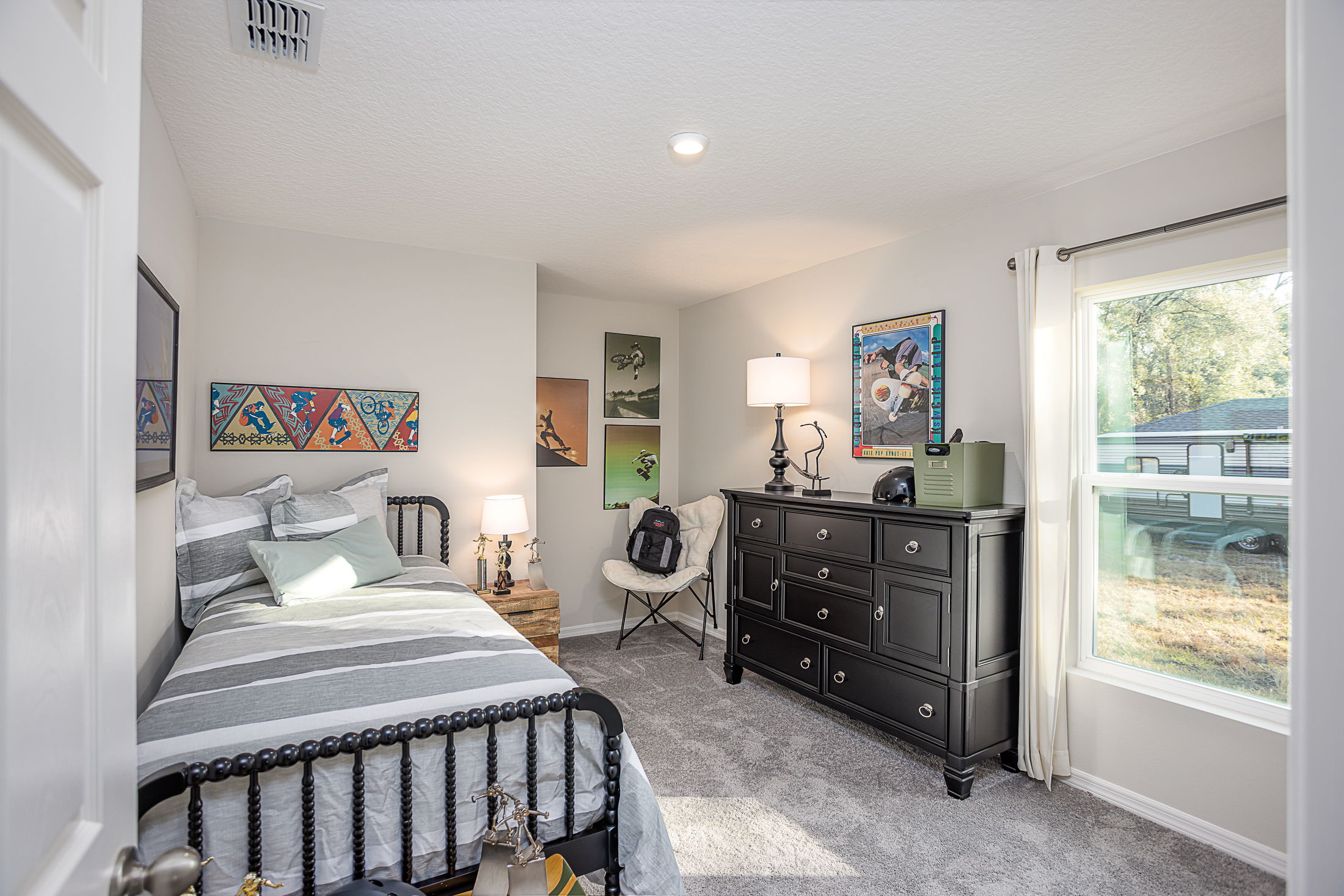 Stylish modern bedroom with a gray metal bed, decorative wall art, and a black dresser near a sunlit window.