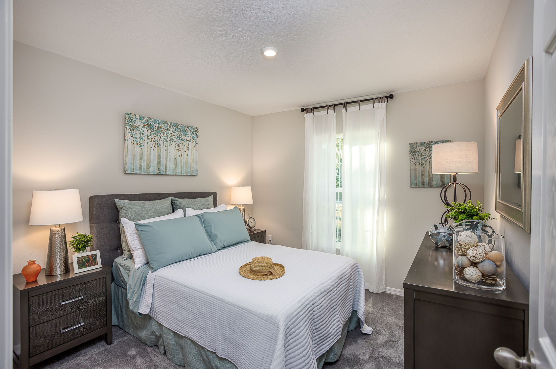 Modern bedroom with a neatly made bed, teal pillows, bedside tables, decorative items, and soft lamp lighting.