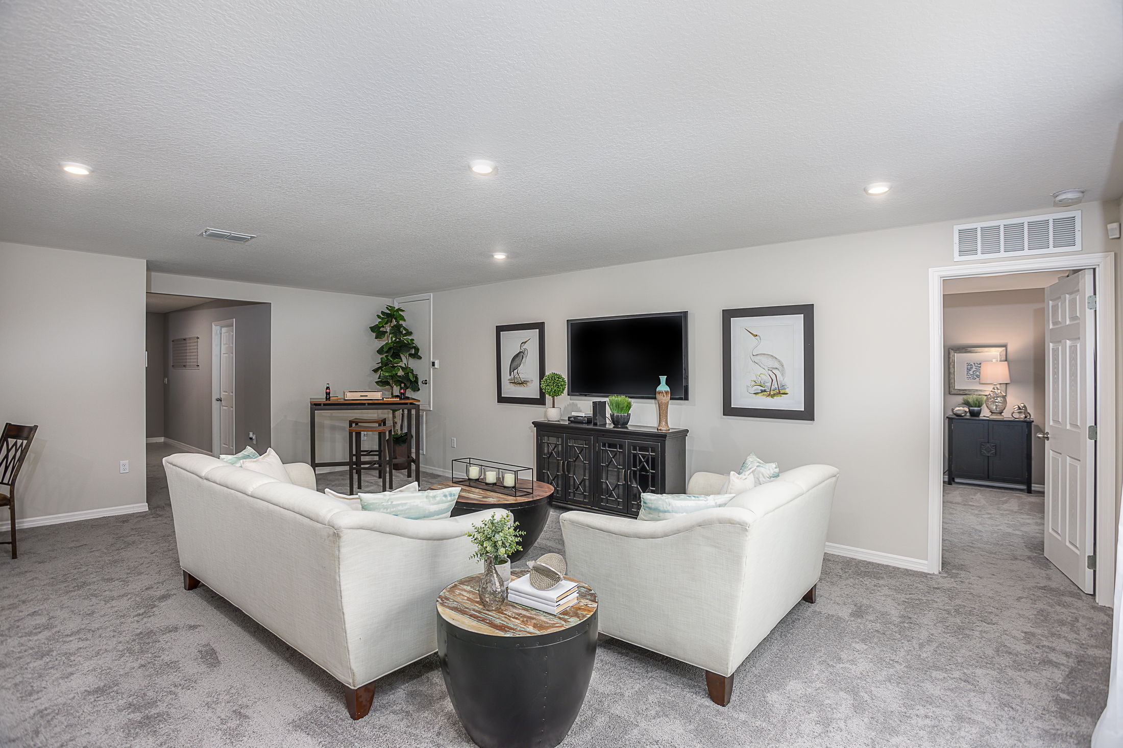 Spacious modern living room with white sofas, a mounted TV, and elegant decor including framed bird art and green plants.