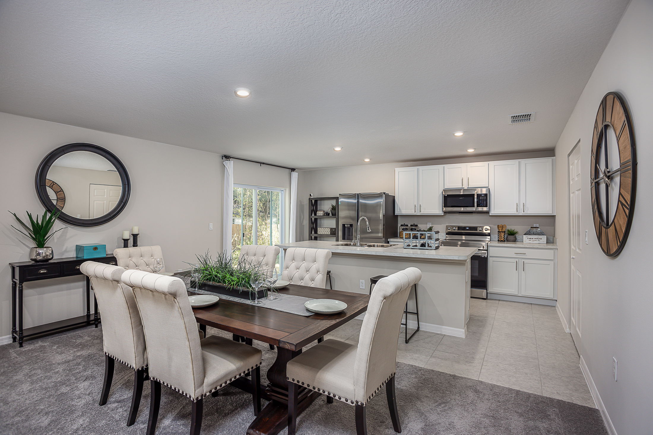 Modern open-plan kitchen and dining area with white cabinets, stainless steel appliances, and elegant upholstered chairs around a wooden table.