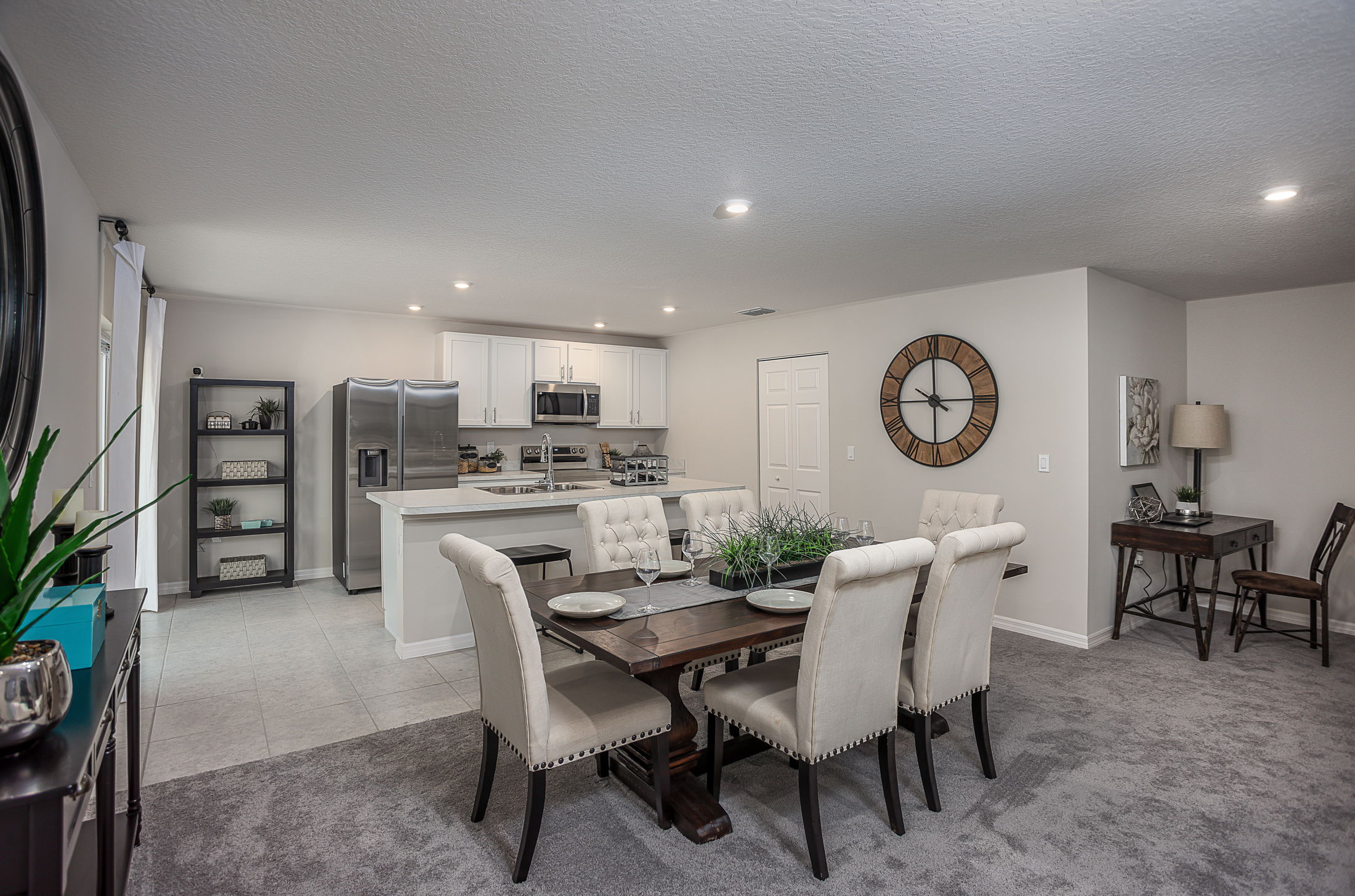 Modern open-concept dining and kitchen area featuring a dark wooden table with beige upholstered chairs, a kitchen with stainless steel appliances, and minimalist décor.