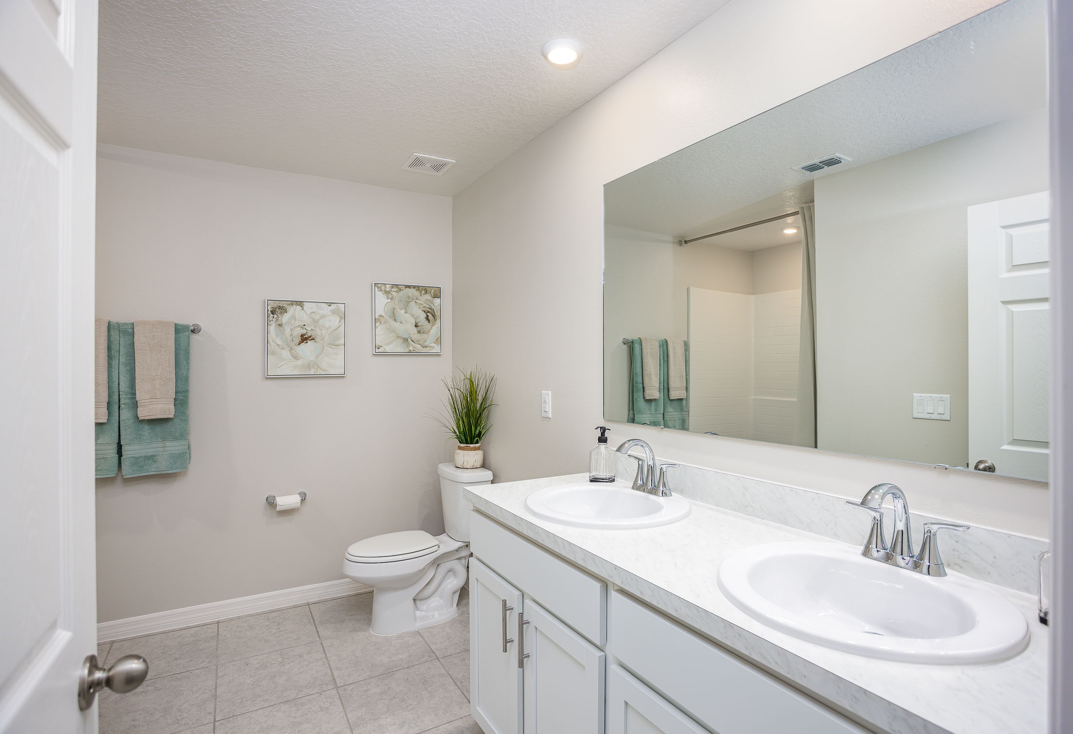 Modern bathroom with dual sinks, large mirror, floral wall art, and minimalist decor.