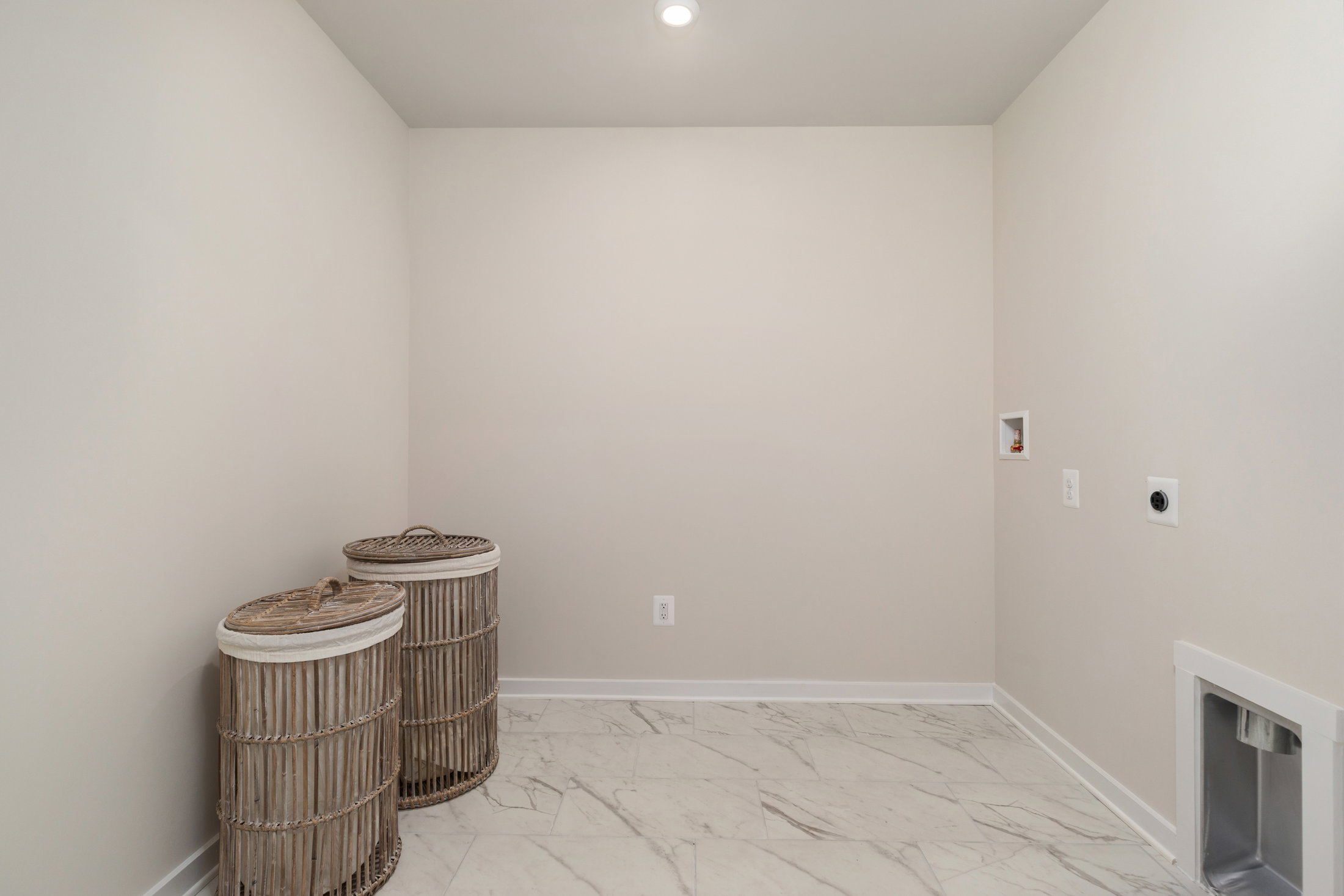 A clean and empty laundry room featuring two woven baskets and light-colored walls with marble flooring.