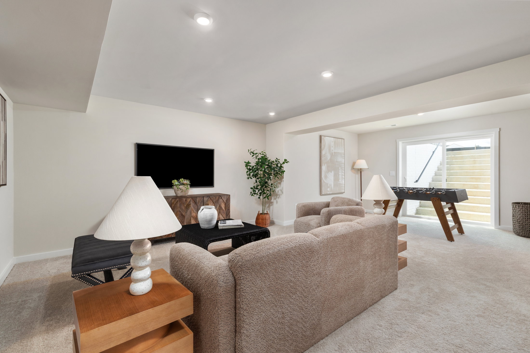 A cozy living room with a beige sofa, a coffee table, a flat-screen TV on the wall, and access to an outdoor area with stairs.