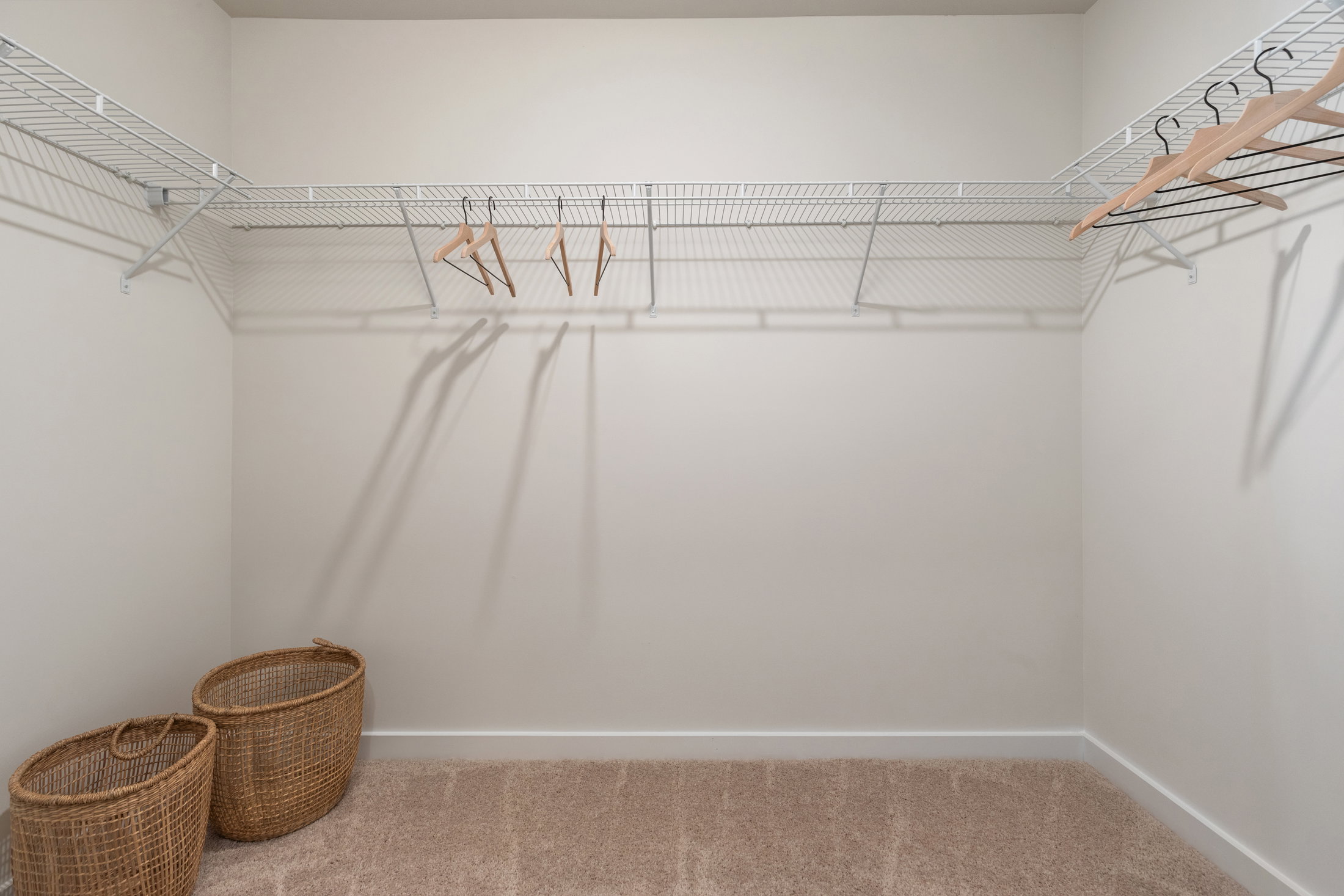 Empty closet interior with wire shelves, wooden hangers, and two wicker baskets on the floor.