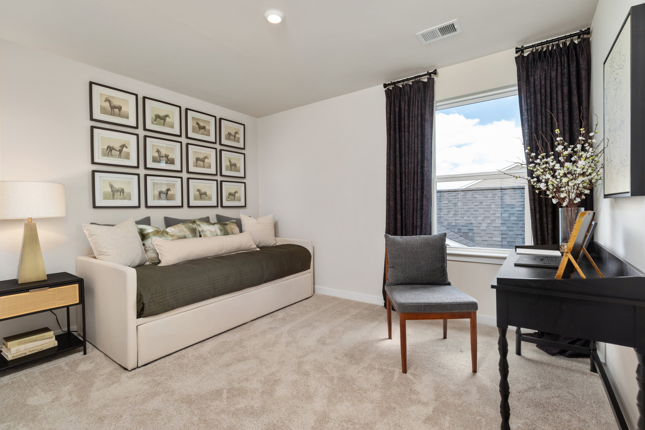 A cozy bedroom featuring a daybed with decorative pillows, a black desk with a chair, and framed artwork on the wall.