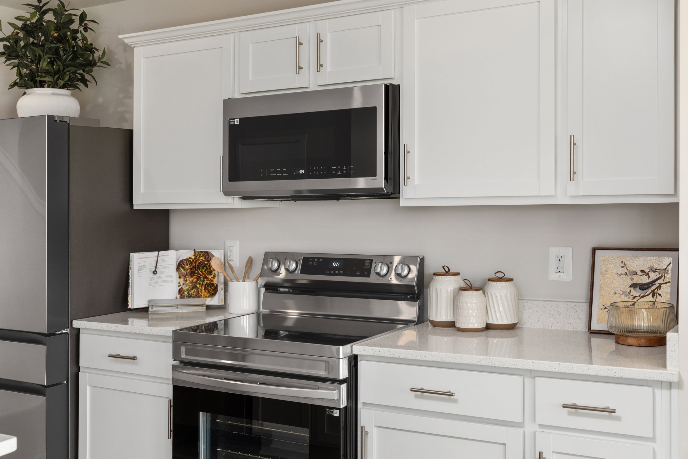 A modern kitchen featuring white cabinets, stainless steel appliances, and a countertop with cooking utensils and decorative items.