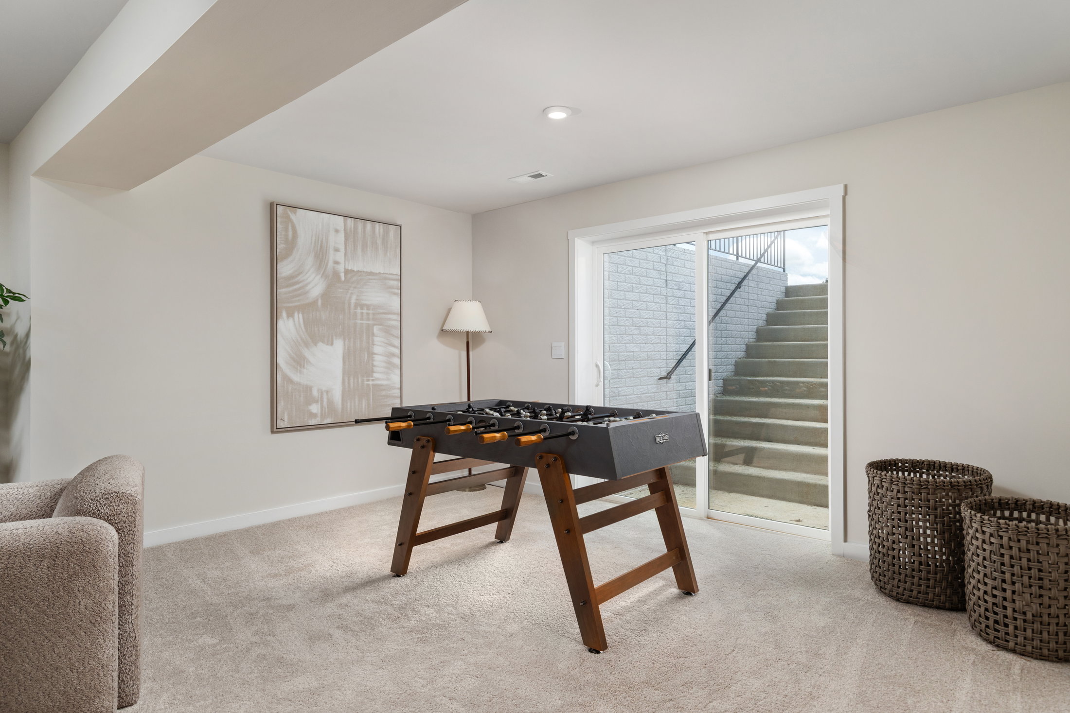 A foosball table in a well-lit room with a staircase visible through a sliding glass door.