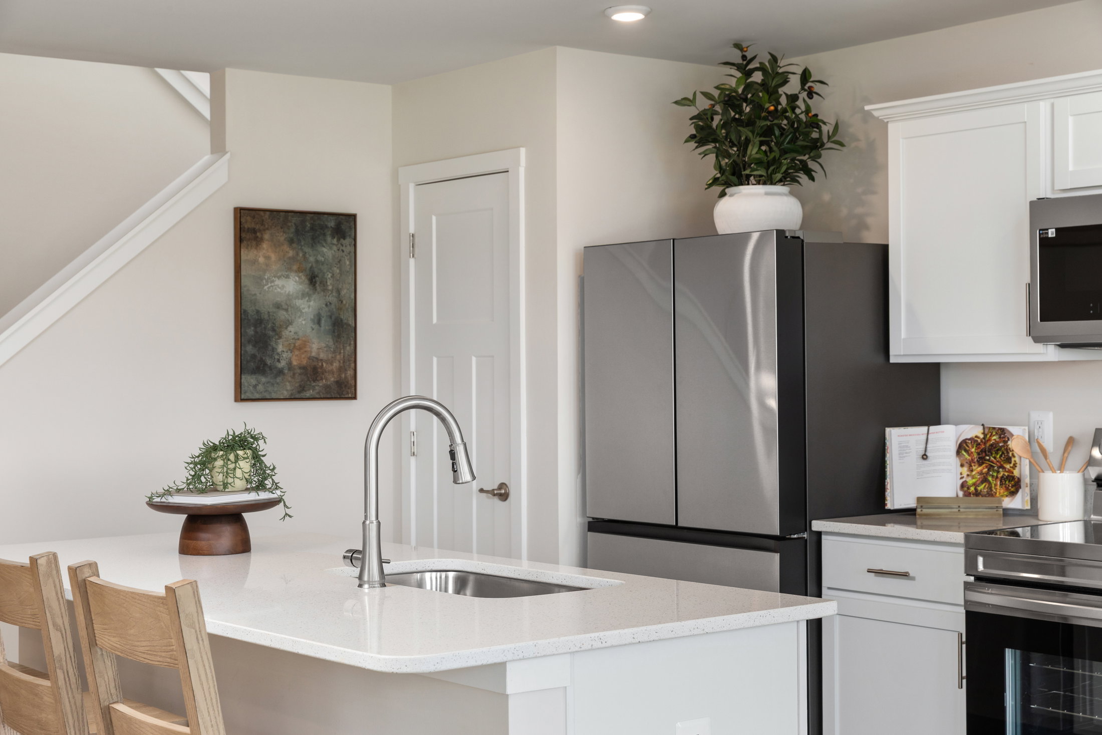 Modern kitchen featuring a sleek black refrigerator, white cabinetry, and an island with a sink and decorative plant.