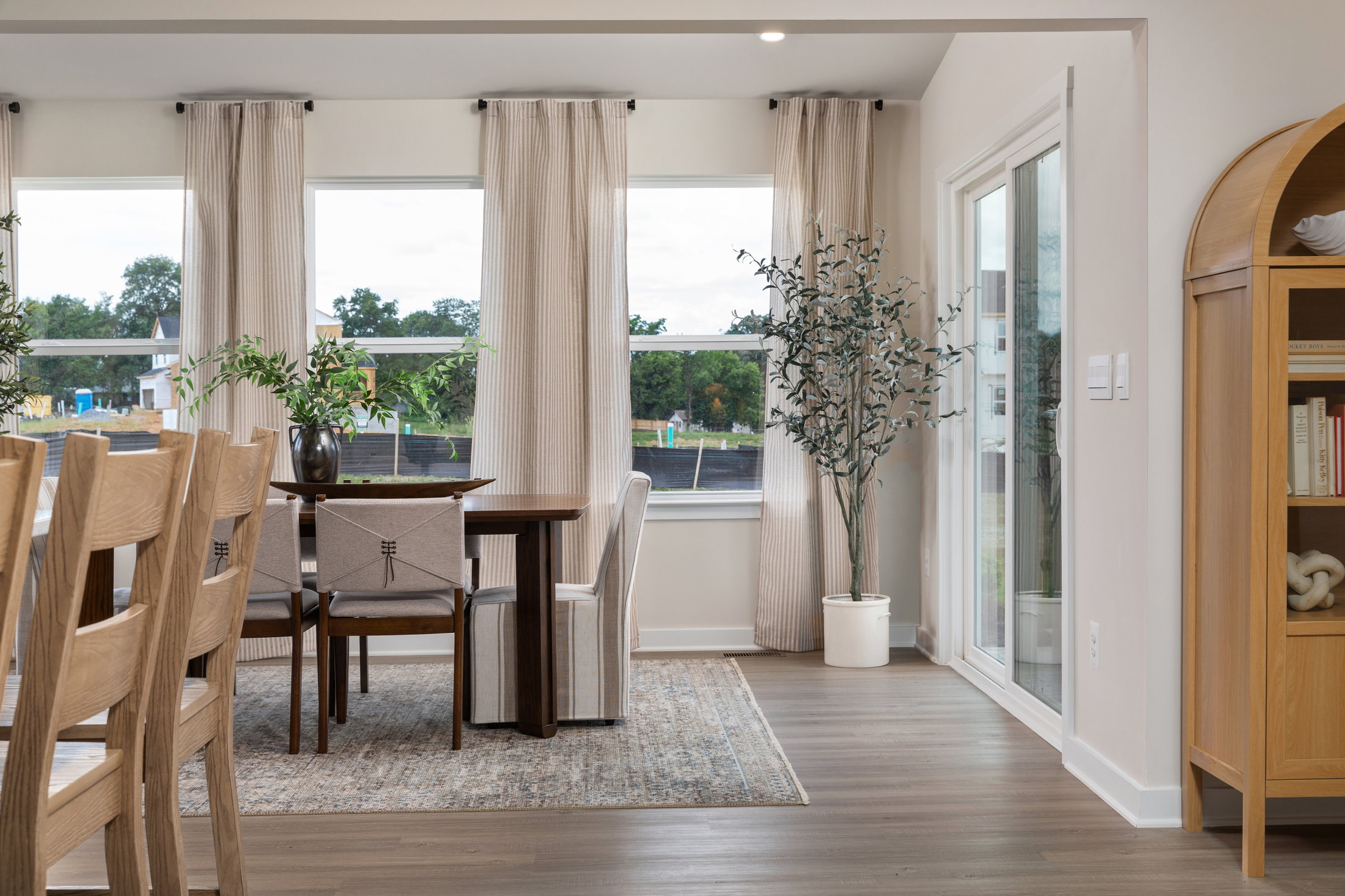 Modern dining area featuring a wooden table, upholstered chairs, and large windows with sheer curtains.
