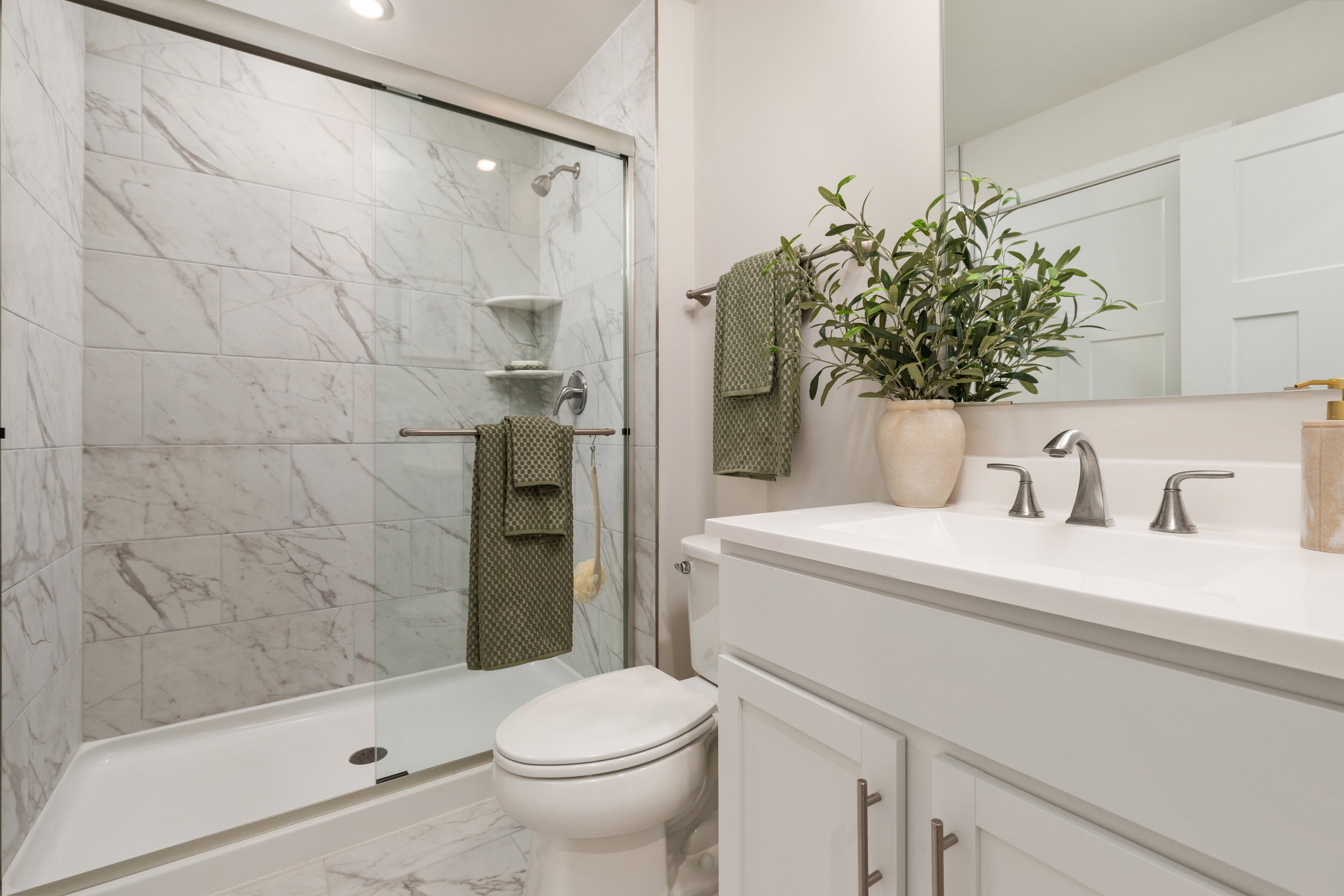 Modern bathroom with a glass shower, marble walls, a white vanity, and a potted plant.
