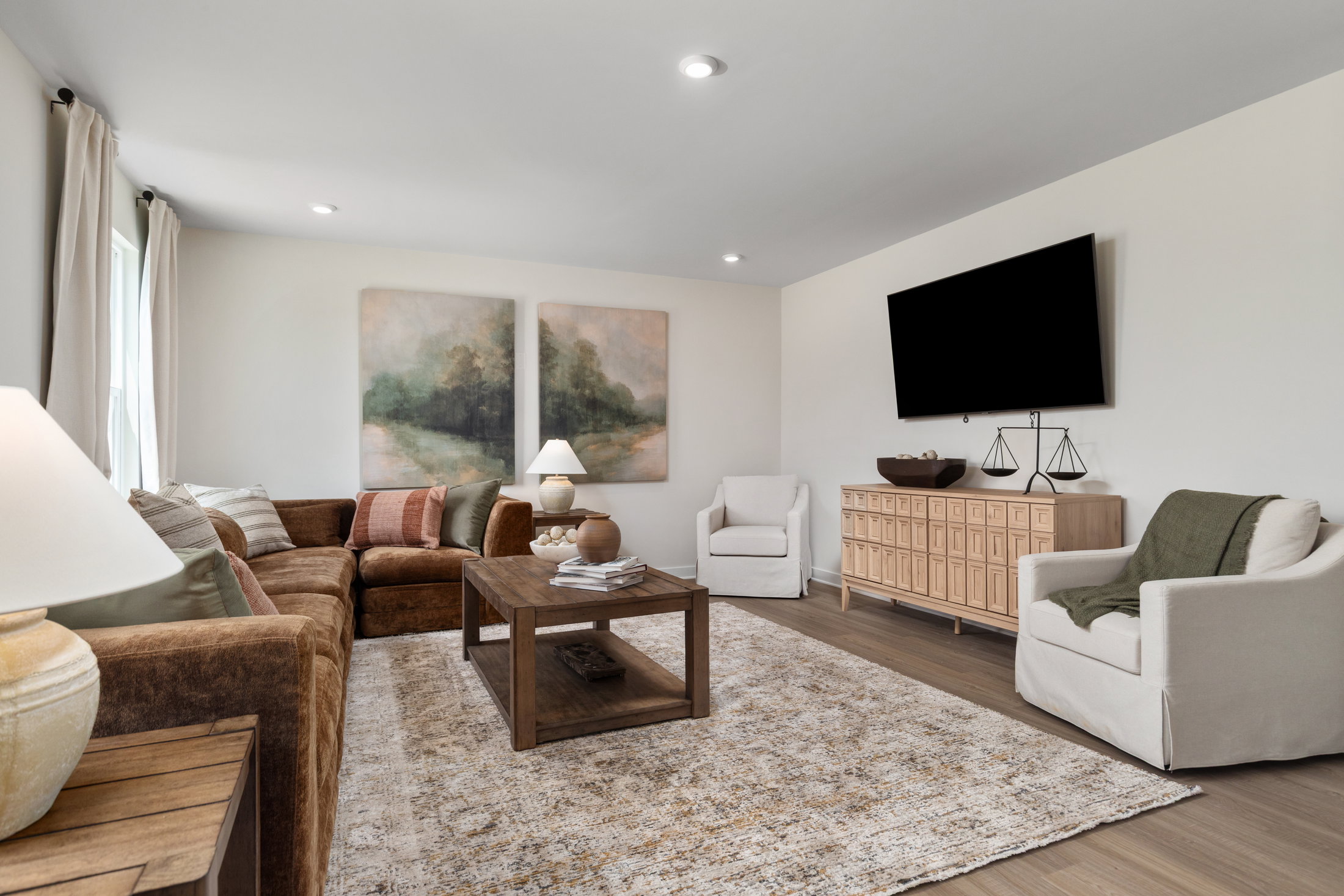 Cozy living room with a brown sectional sofa, two chairs, a wooden coffee table, and abstract wall art.