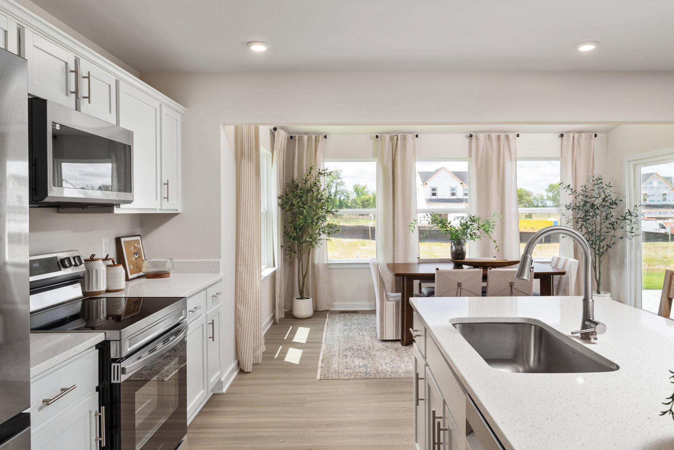 Modern kitchen featuring white cabinets, stainless steel appliances, and a dining area with large windows.