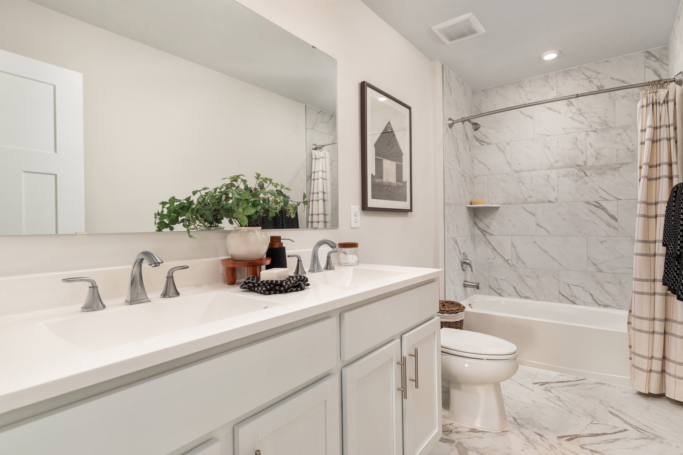 A modern bathroom featuring a double sink vanity, a large mirror, a bathtub with a shower, and marble tile walls.