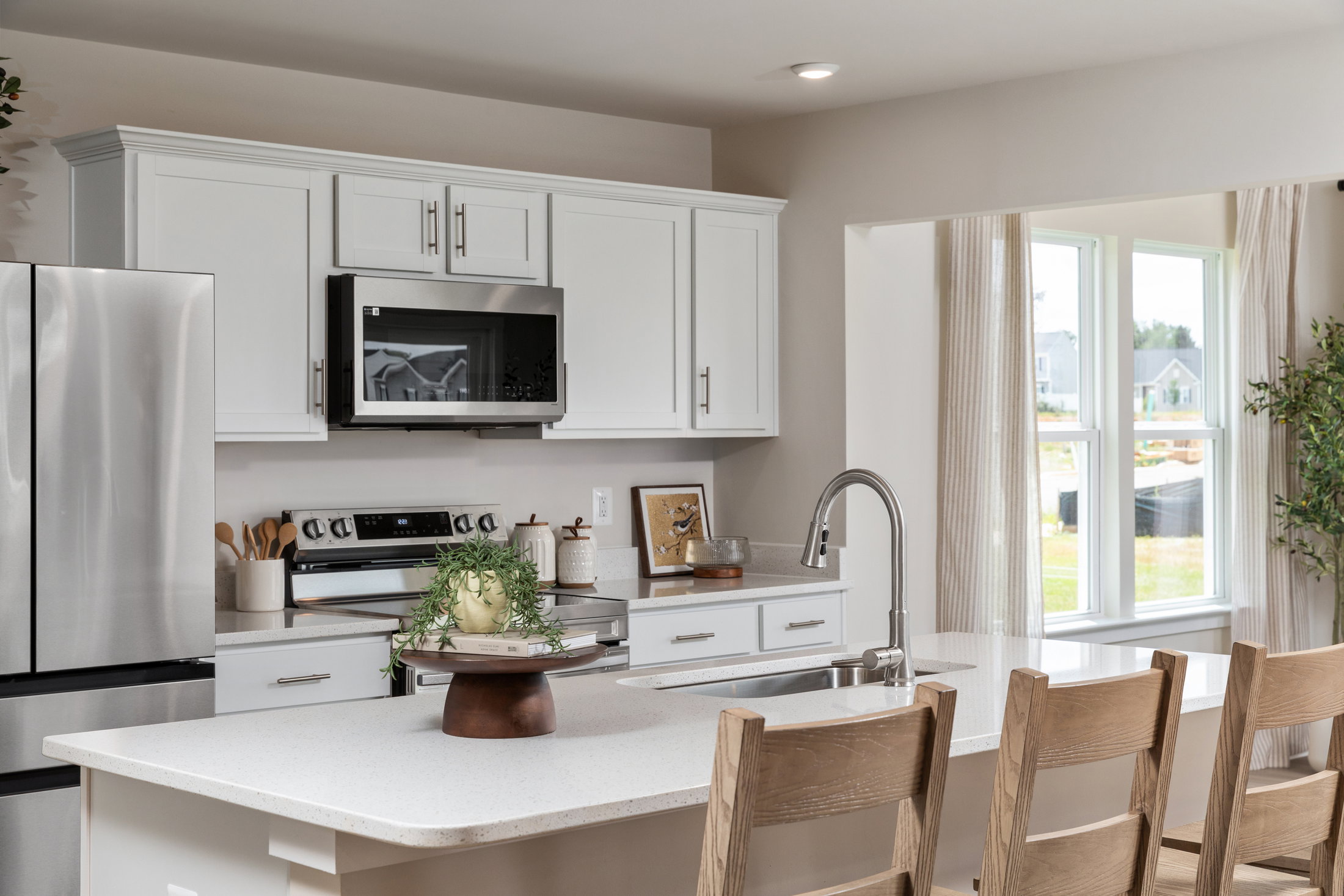 Modern kitchen featuring white cabinets, stainless steel appliances, a large island with seating, and a view of the outdoors through a window.