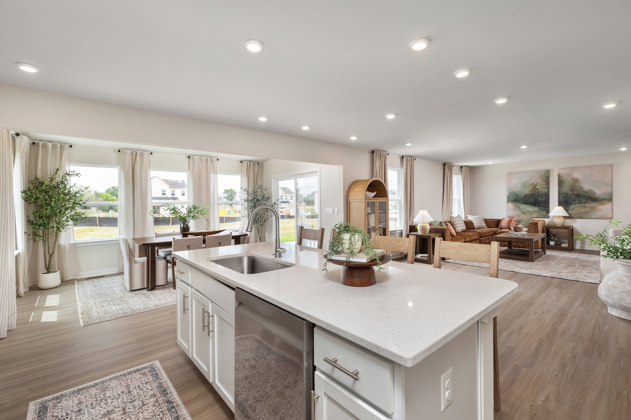 Modern open-concept living space featuring a kitchen island with sink, hardwood floors, large windows, and a comfortable seating area.