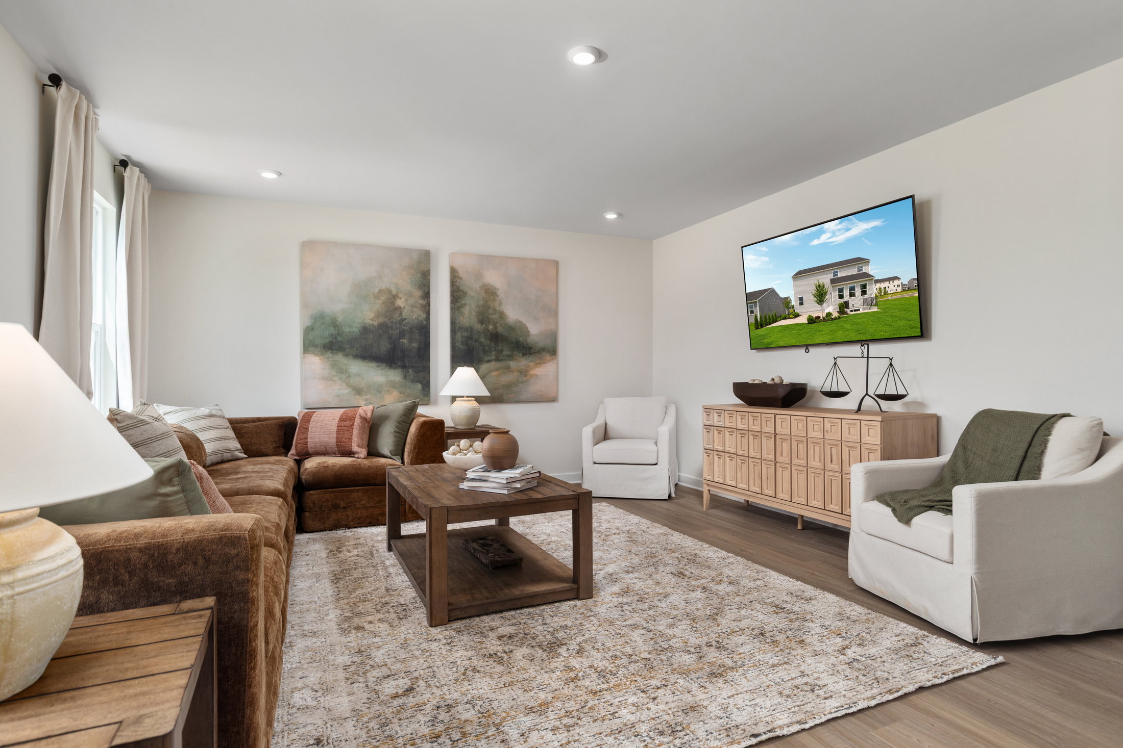 A modern living room featuring a brown sofa, two armchairs, a wooden coffee table, and a large TV mounted on the wall with artwork displayed.