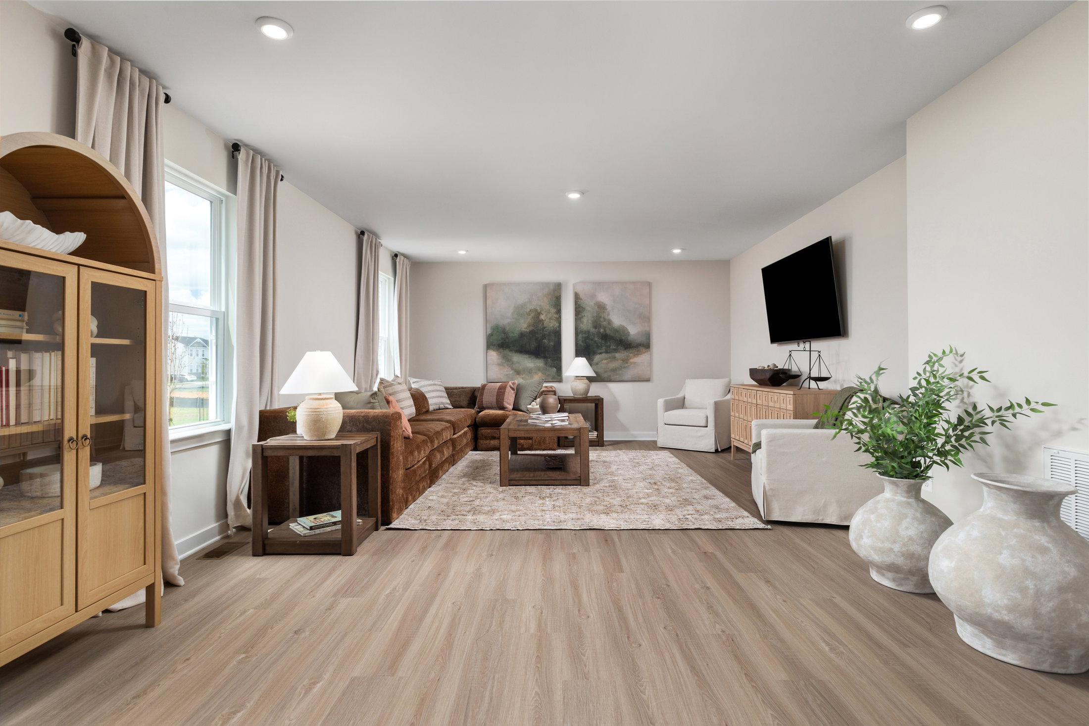 A modern living room featuring a brown sofa, white armchair, coffee table, and large decorative vases on a wooden floor.