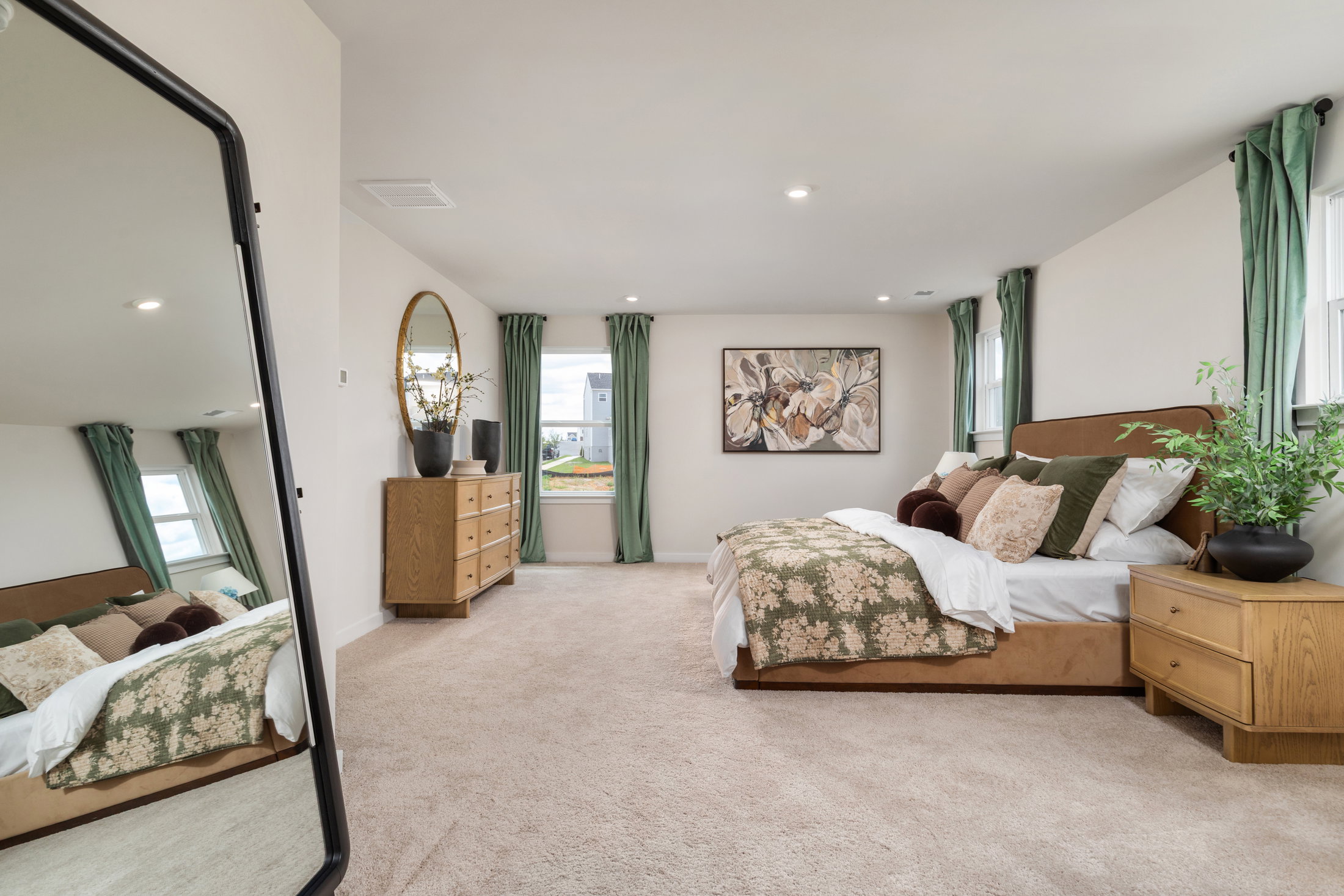 A cozy bedroom featuring a large mirror, a bed with decorative pillows, a wooden dresser, and a wall art piece.