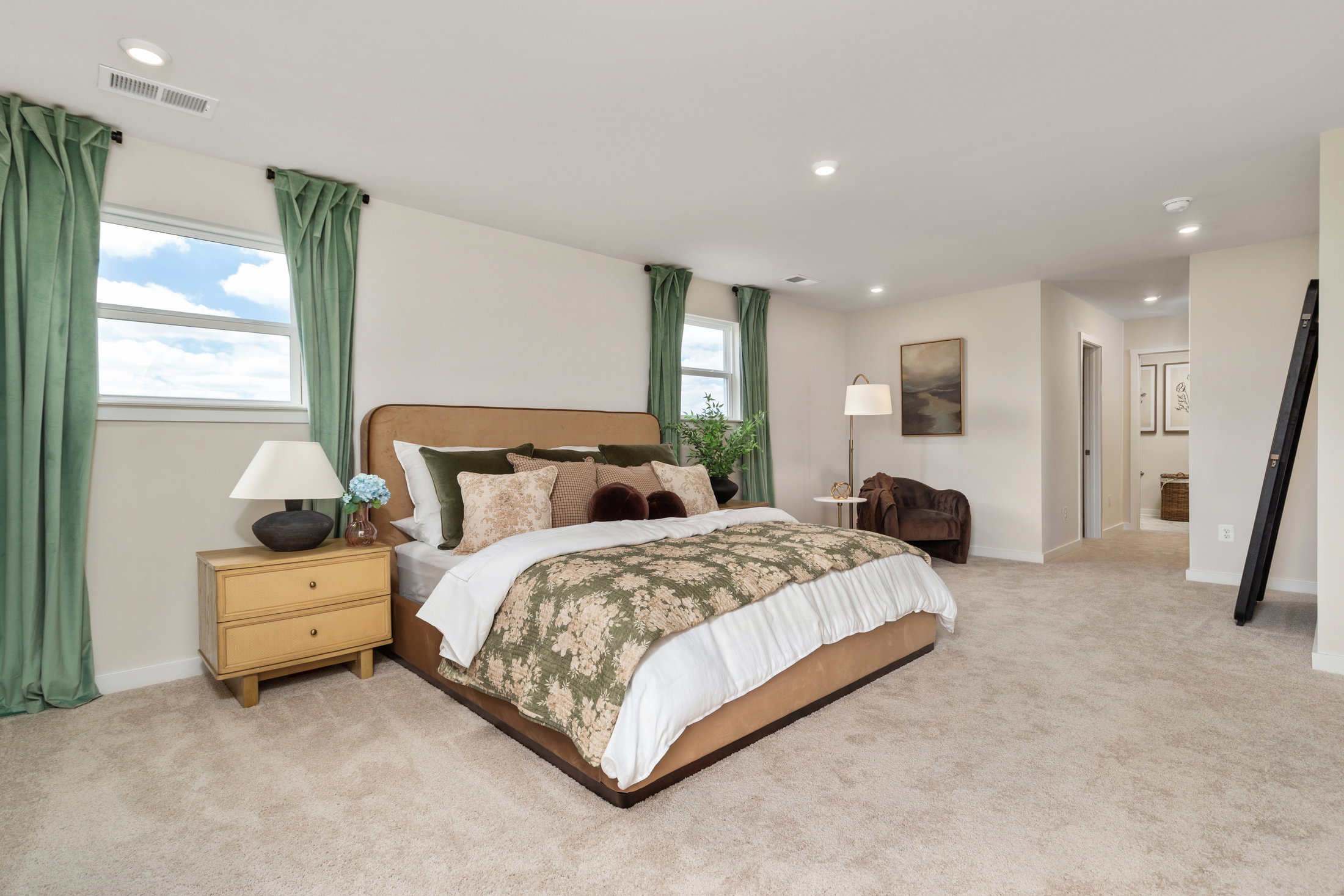 A cozy bedroom featuring a bed with decorative pillows, a wooden nightstand with a lamp, and soft green curtains.