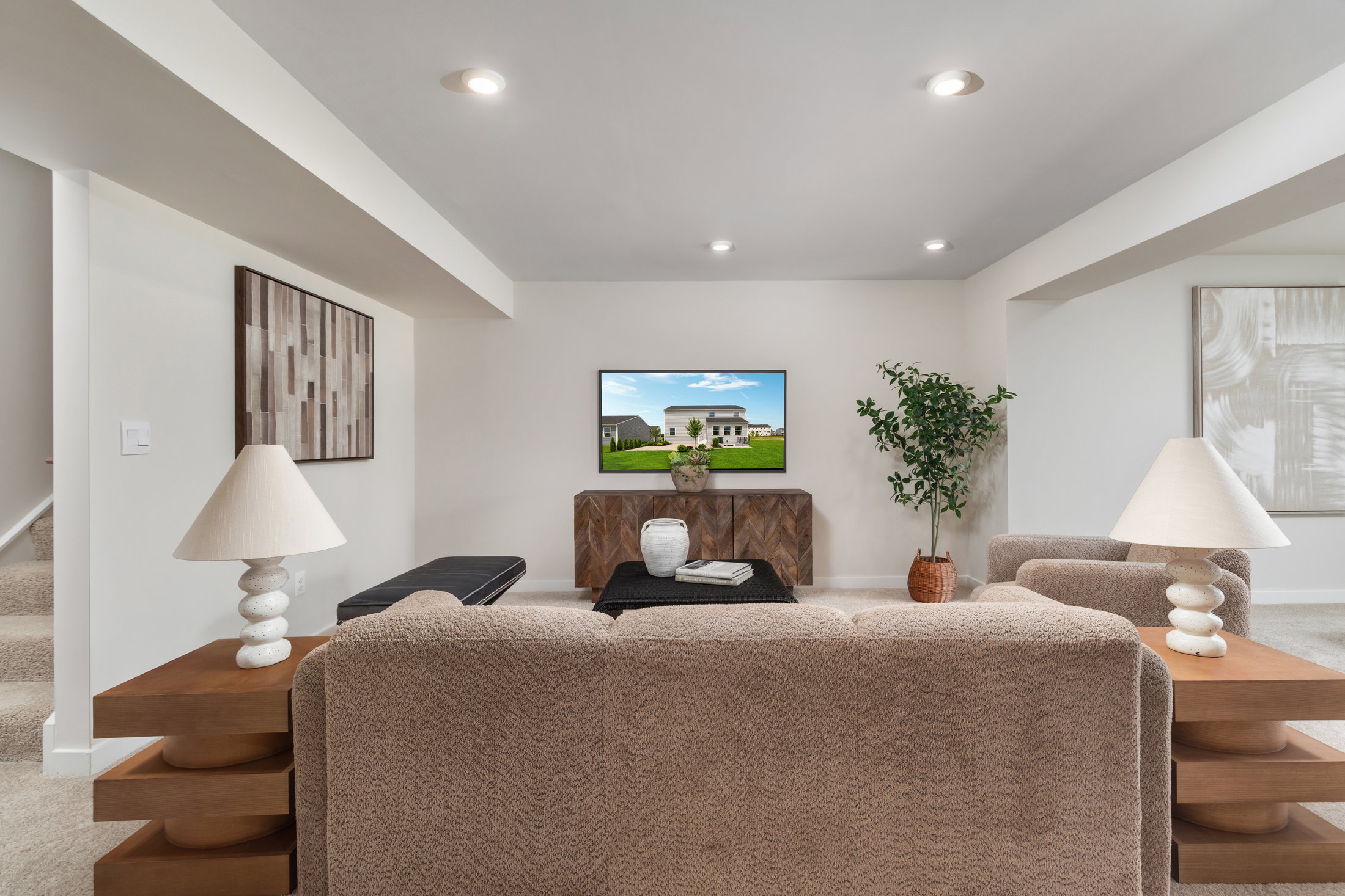 A cozy living room with a beige sofa, two lamps, a coffee table, and a television displaying a home exterior.