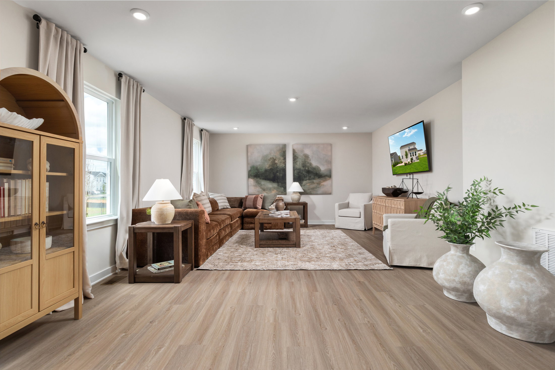 A modern living room with a brown sofa, an armchair, a wooden cabinet, and large abstract artworks on the walls.