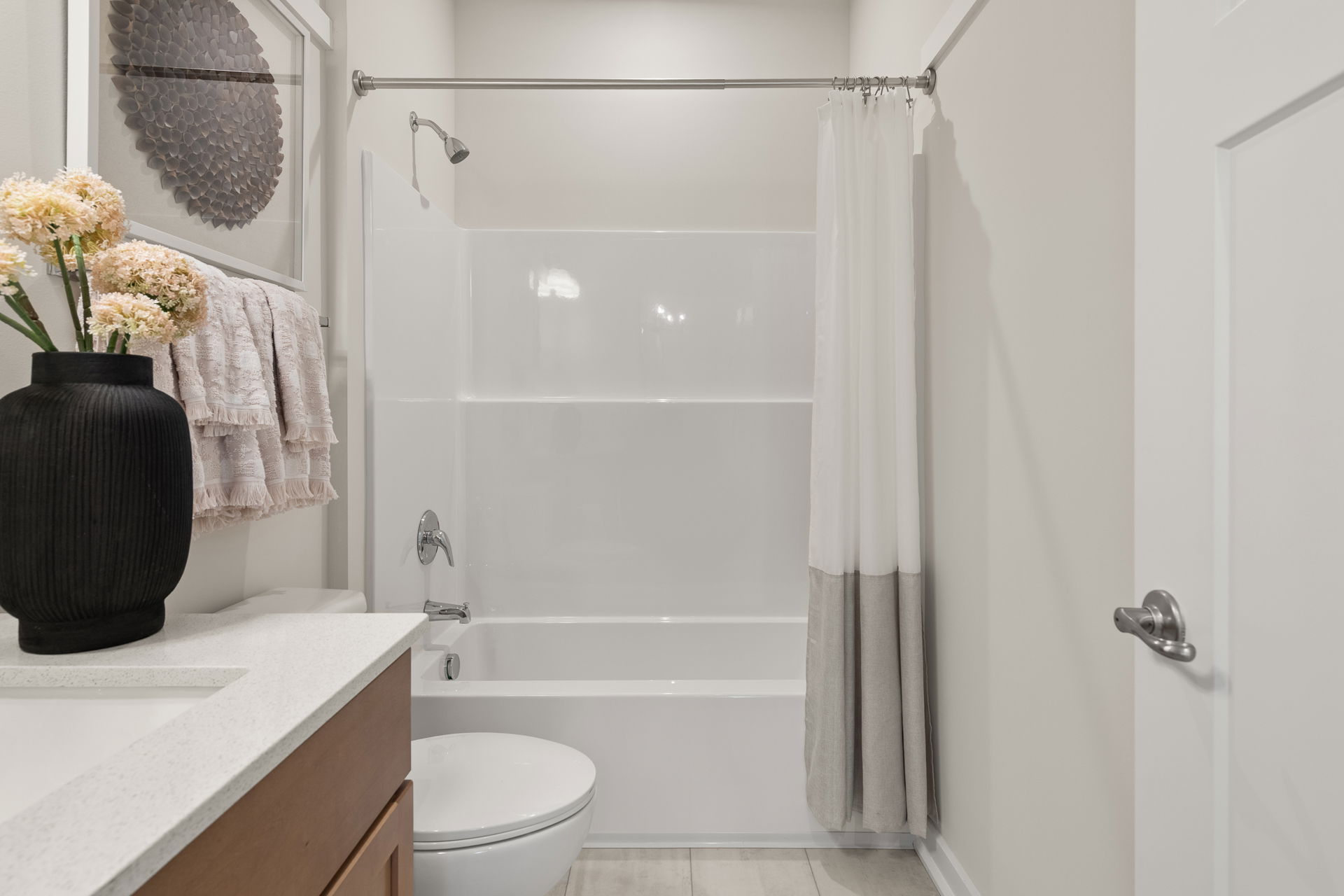 Modern bathroom interior with a white bathtub, shower curtain, black vase on the countertop, and decorative wall art.