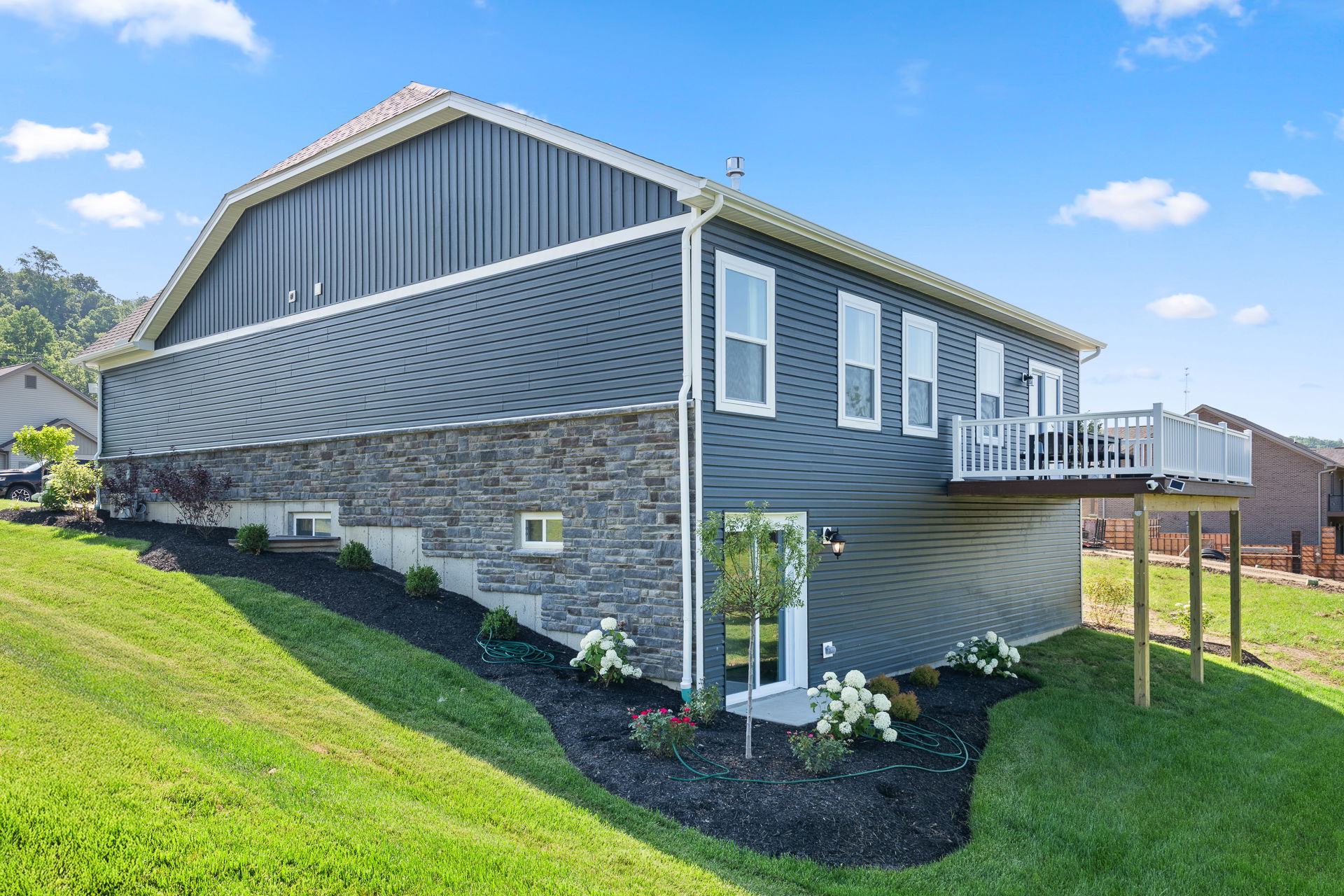 Modern gray house with stone accents, white balcony, and landscaped yard on a sunny day.