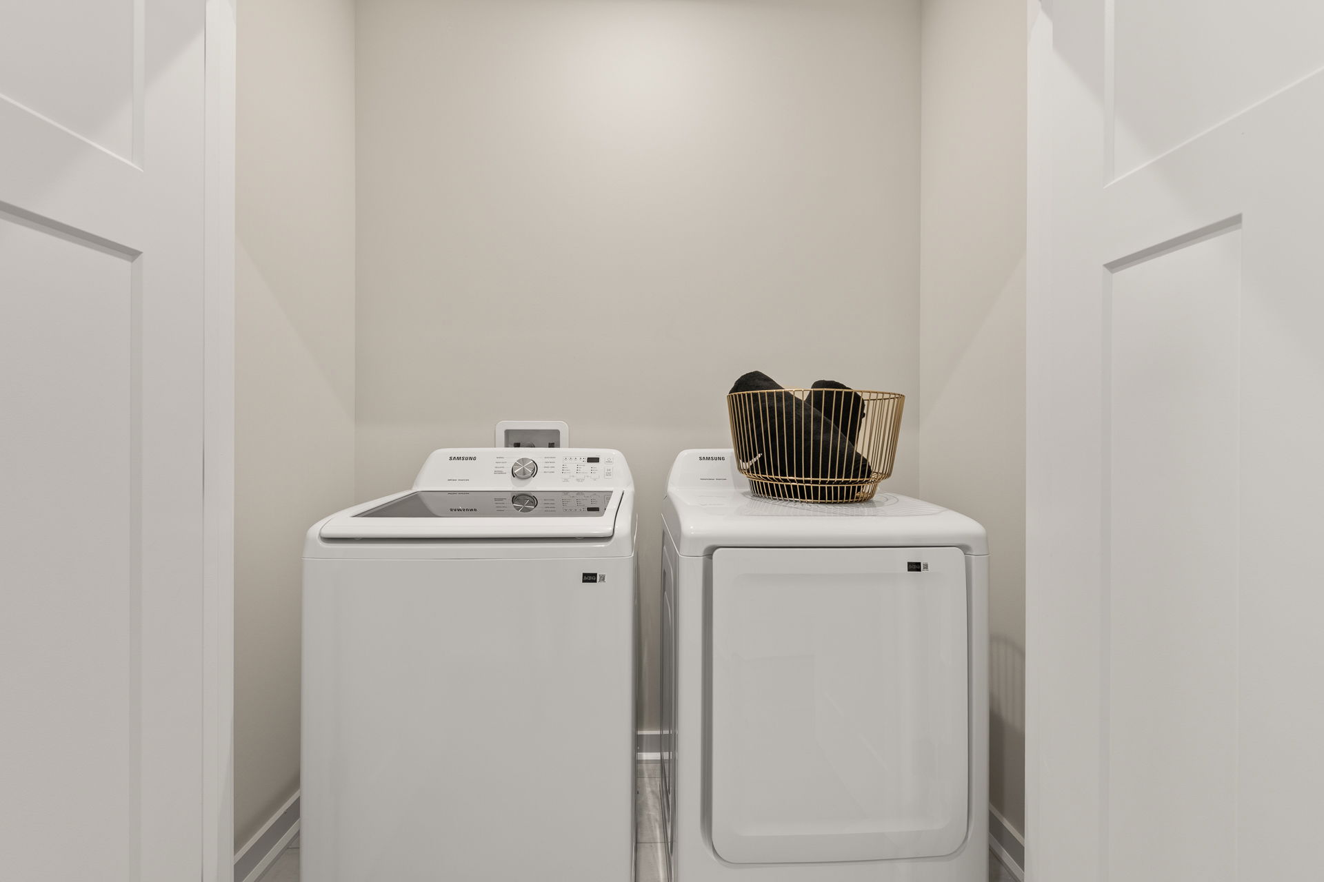 Modern laundry room featuring a Samsung washer and dryer set, with a gold wire basket filled with black items on top.