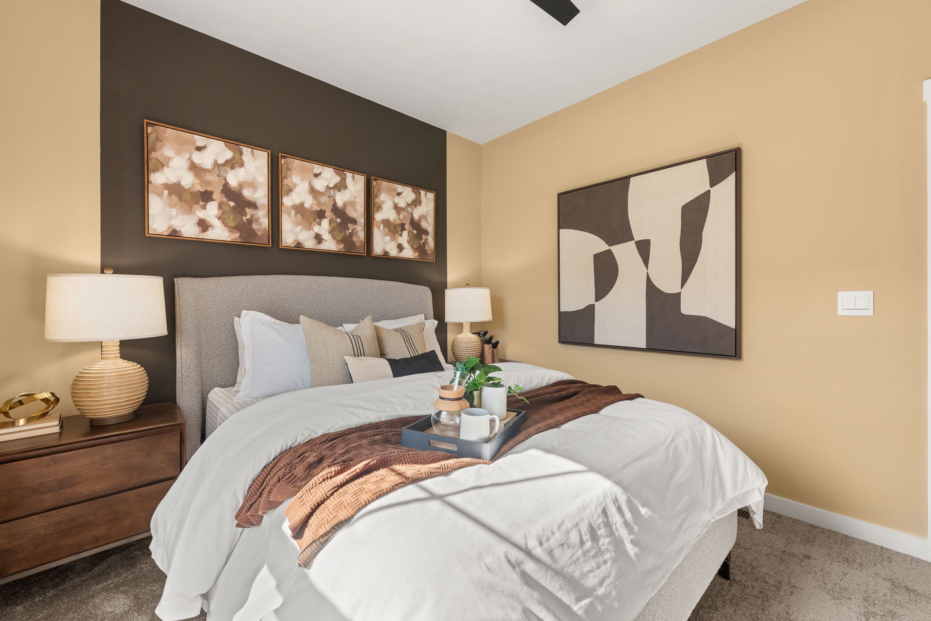 Modern bedroom interior with cozy bed, abstract wall art, and elegant bedside lamps in warm earth tones.
