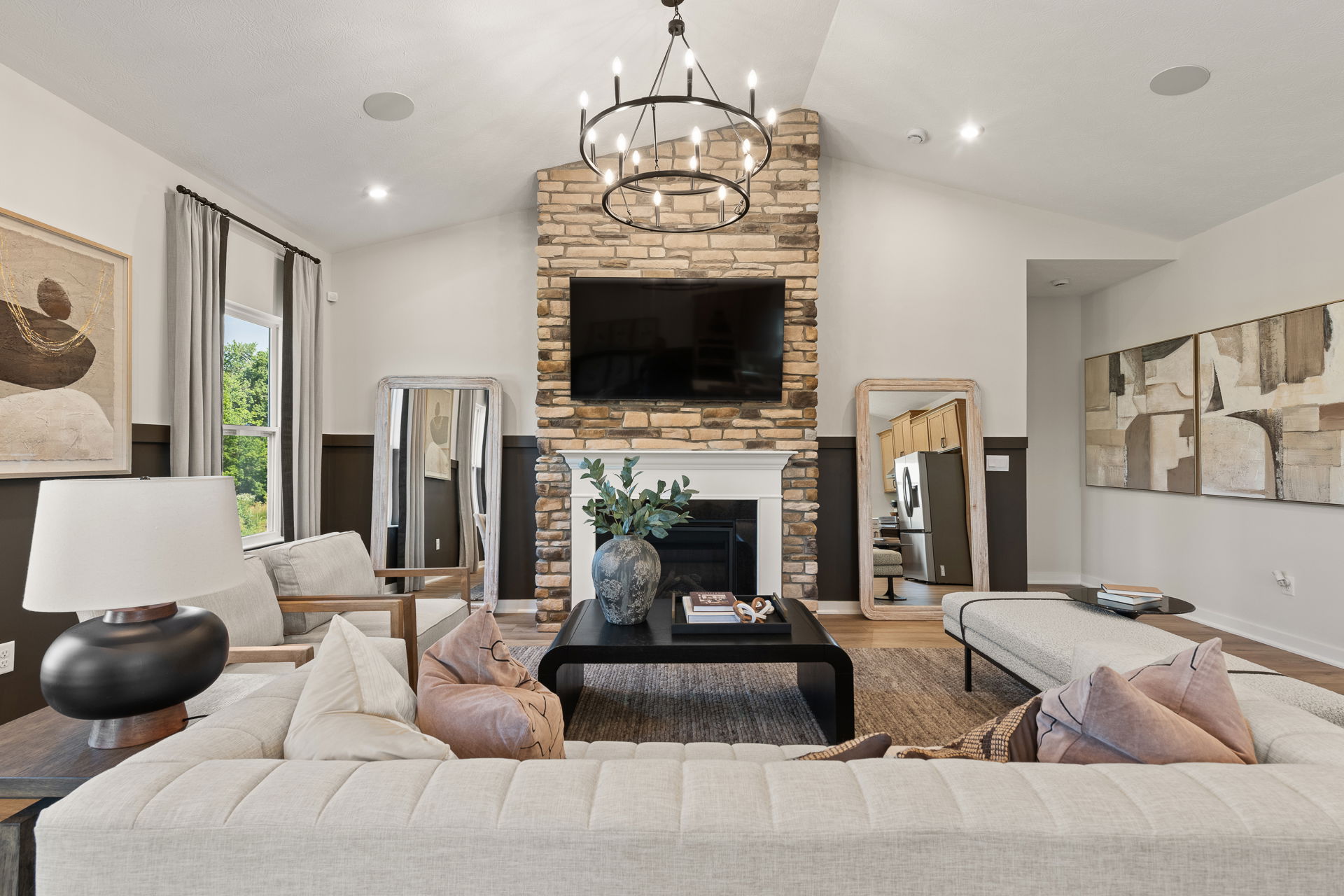 Stylish living room with modern decor featuring a stone fireplace, wall-mounted TV, chic chandelier, and comfortable seating area.