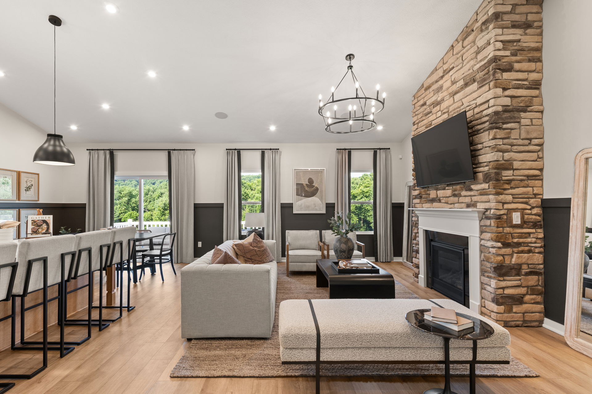 Modern living room featuring a stone fireplace, sleek furniture, and a large chandelier, with an open view to a lush landscape.