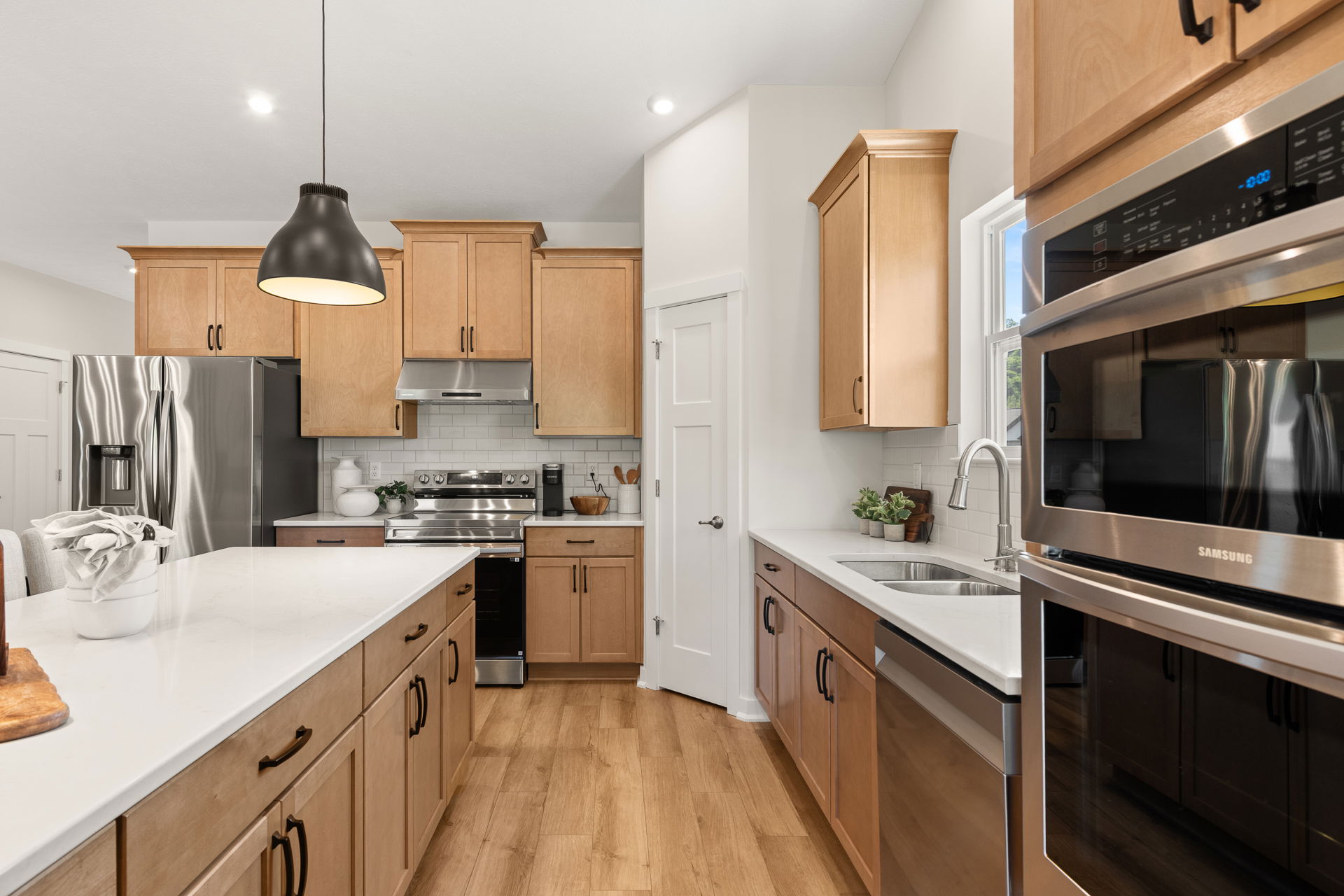 Modern kitchen with wooden cabinets, stainless steel appliances, and a central island under pendant lighting.