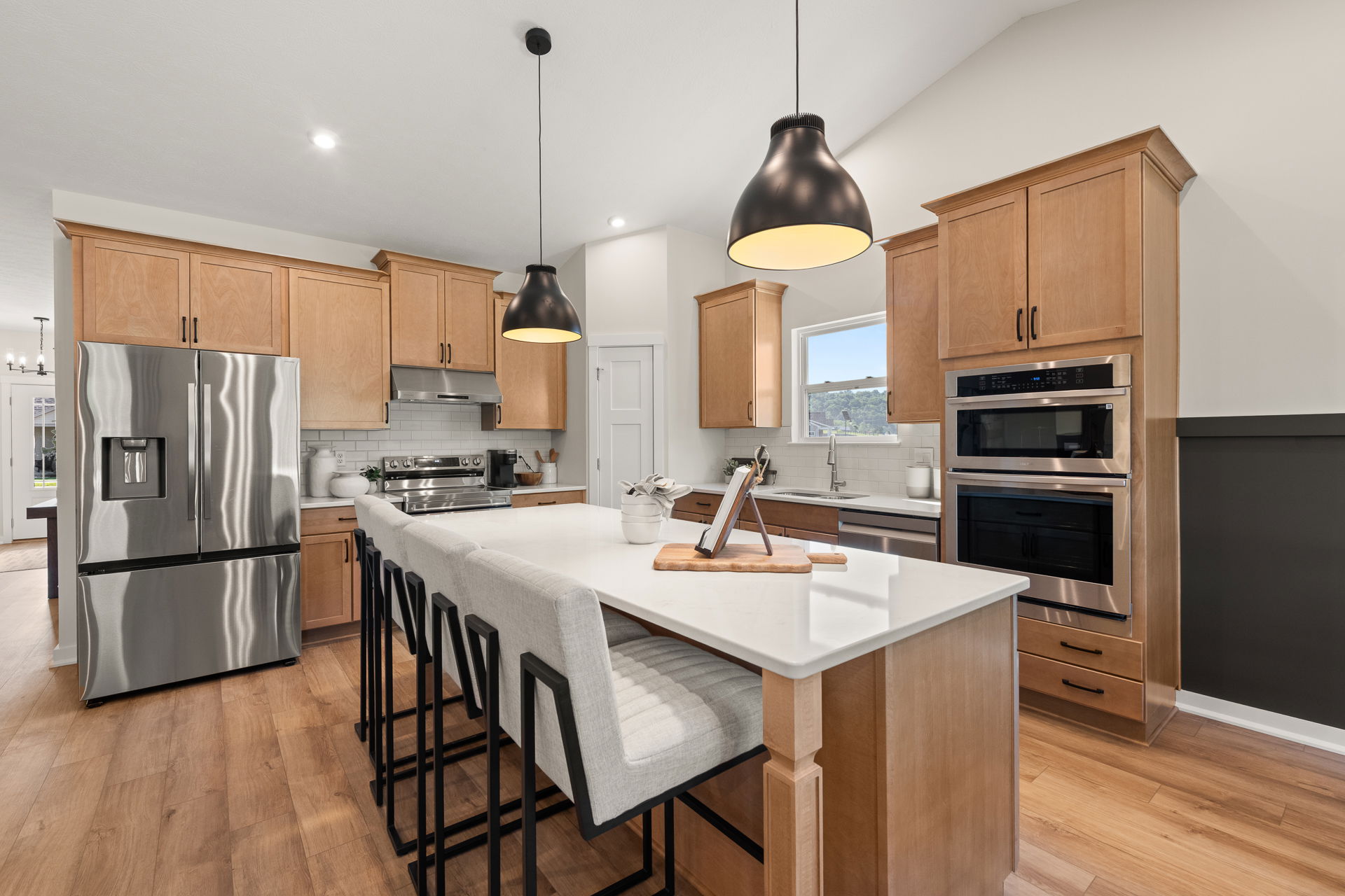Modern kitchen with wooden cabinets, stainless steel appliances, and a large island featuring contemporary pendant lighting and upholstered barstools.