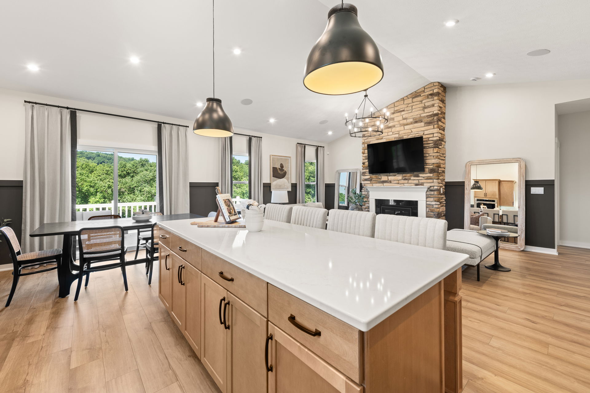Modern open concept kitchen and living room with stone fireplace, large island, and bright natural lighting.