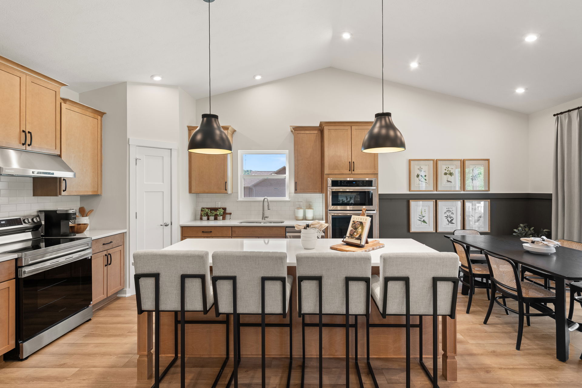 Modern kitchen interior with wooden cabinets, stainless steel appliances, and a large island featuring pendant lighting and stylish bar stools.