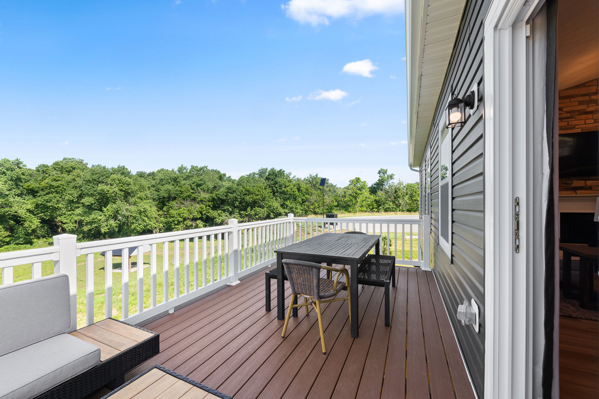 Spacious outdoor deck with a dining table and seating, surrounded by a white railing and overlooking a lush green landscape.