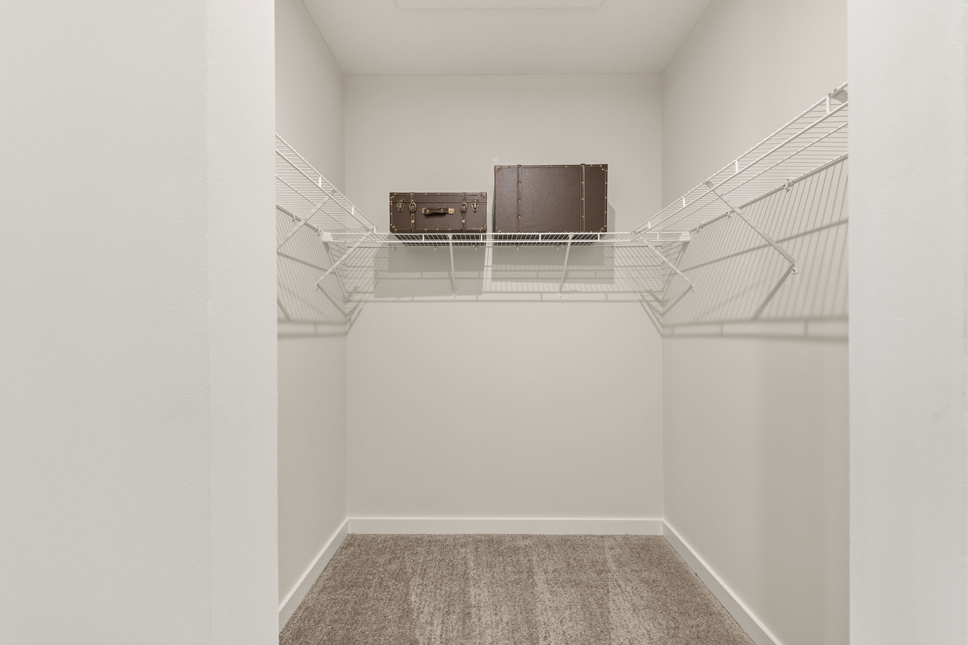 Empty walk-in closet with wire shelves and two vintage suitcases on the top rack.
