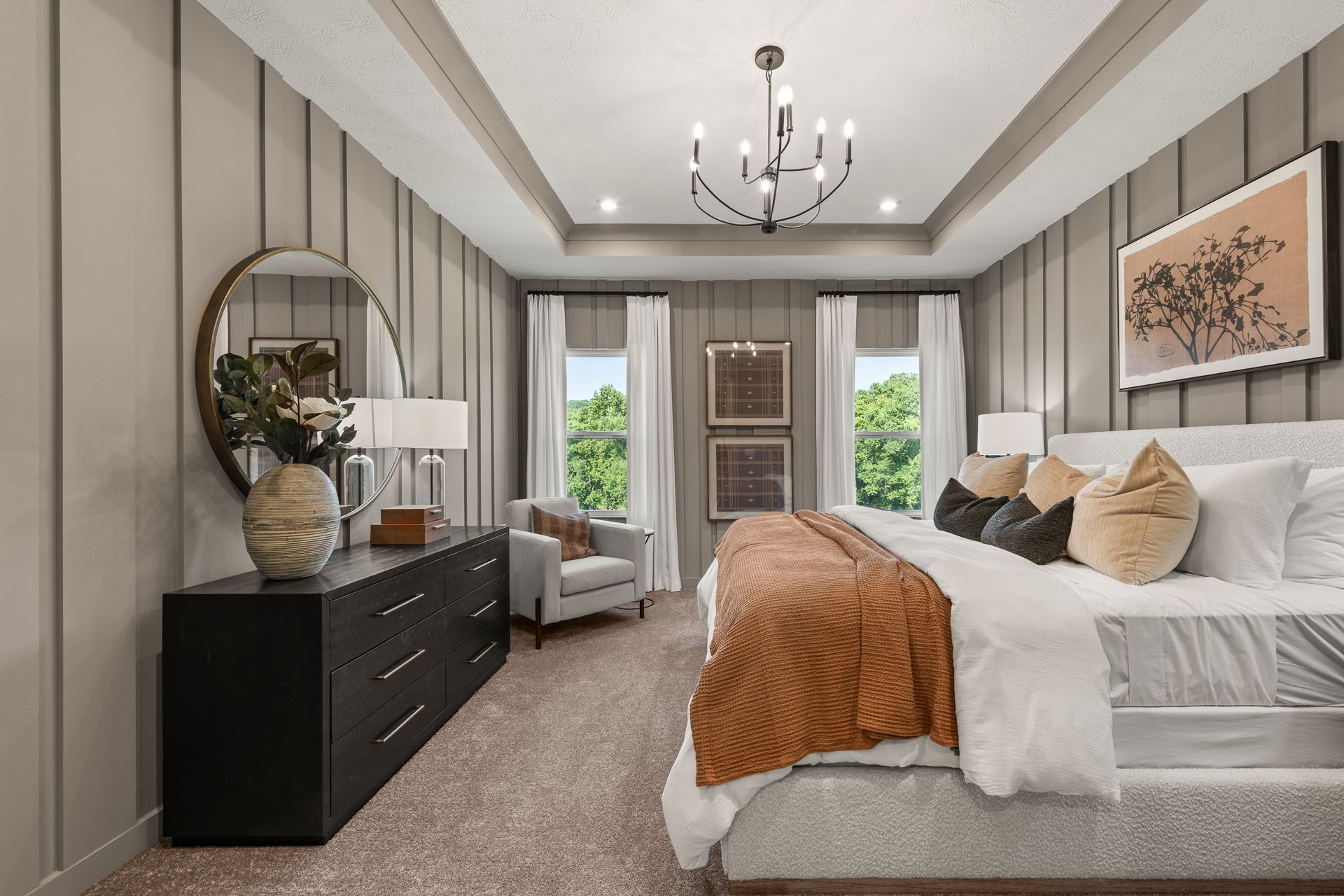 Modern bedroom with elegant decor, featuring a stylish chandelier, paneled walls, comfortable white bed, and large windows with scenic greenery.