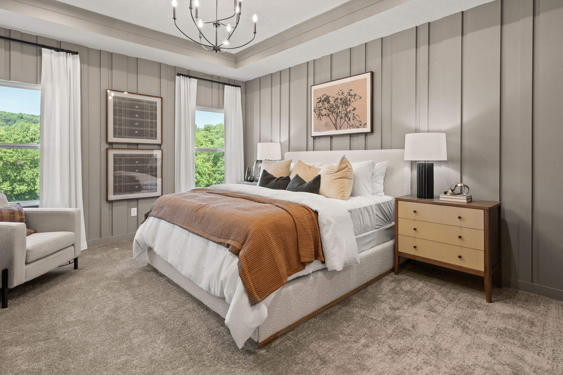 Luxurious bedroom with a cozy bed, modern chandelier, and large windows overlooking lush greenery.