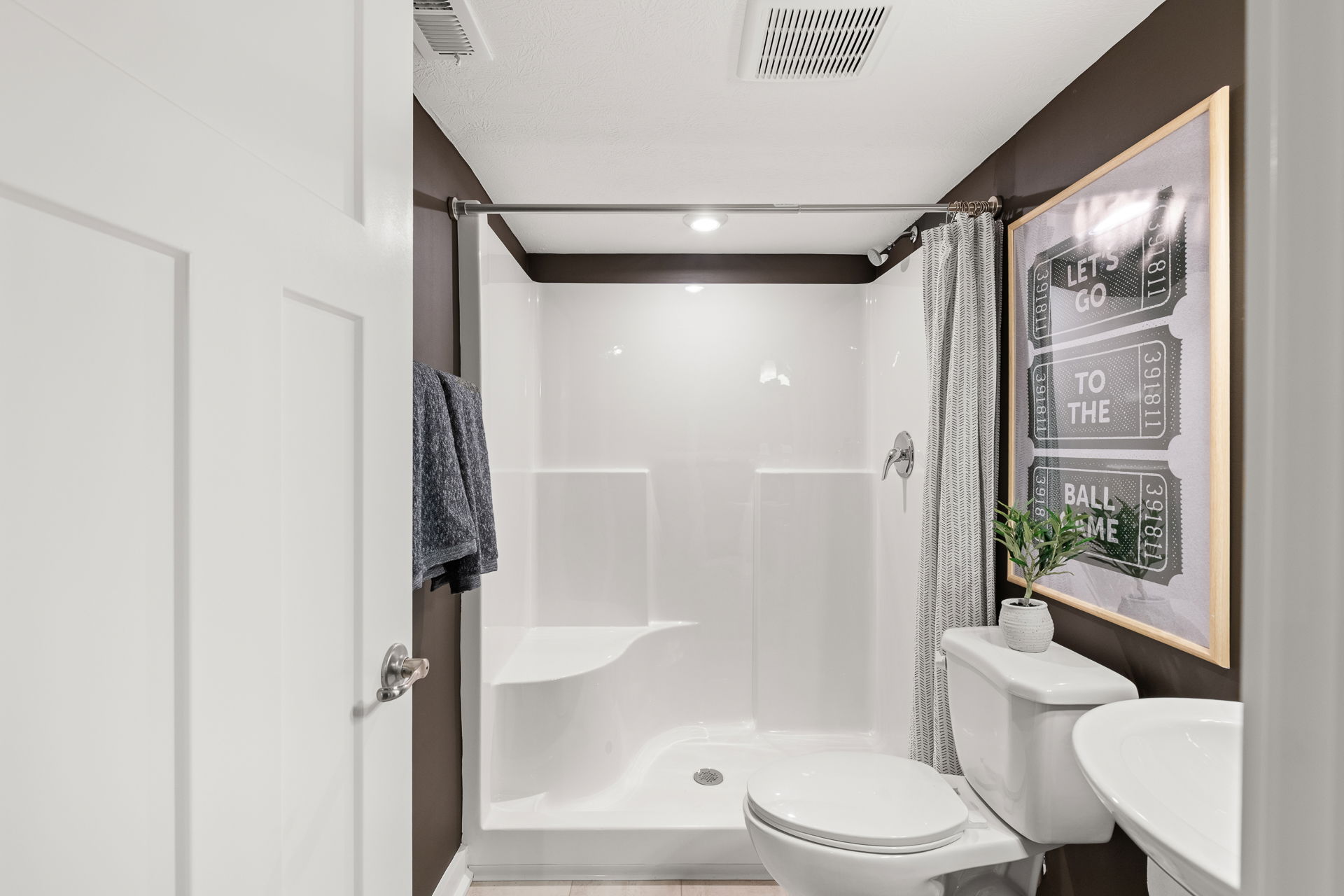 Modern bathroom with a white bathtub and shower curtain, white toilet, sink, framed wall art, and decorative plant.