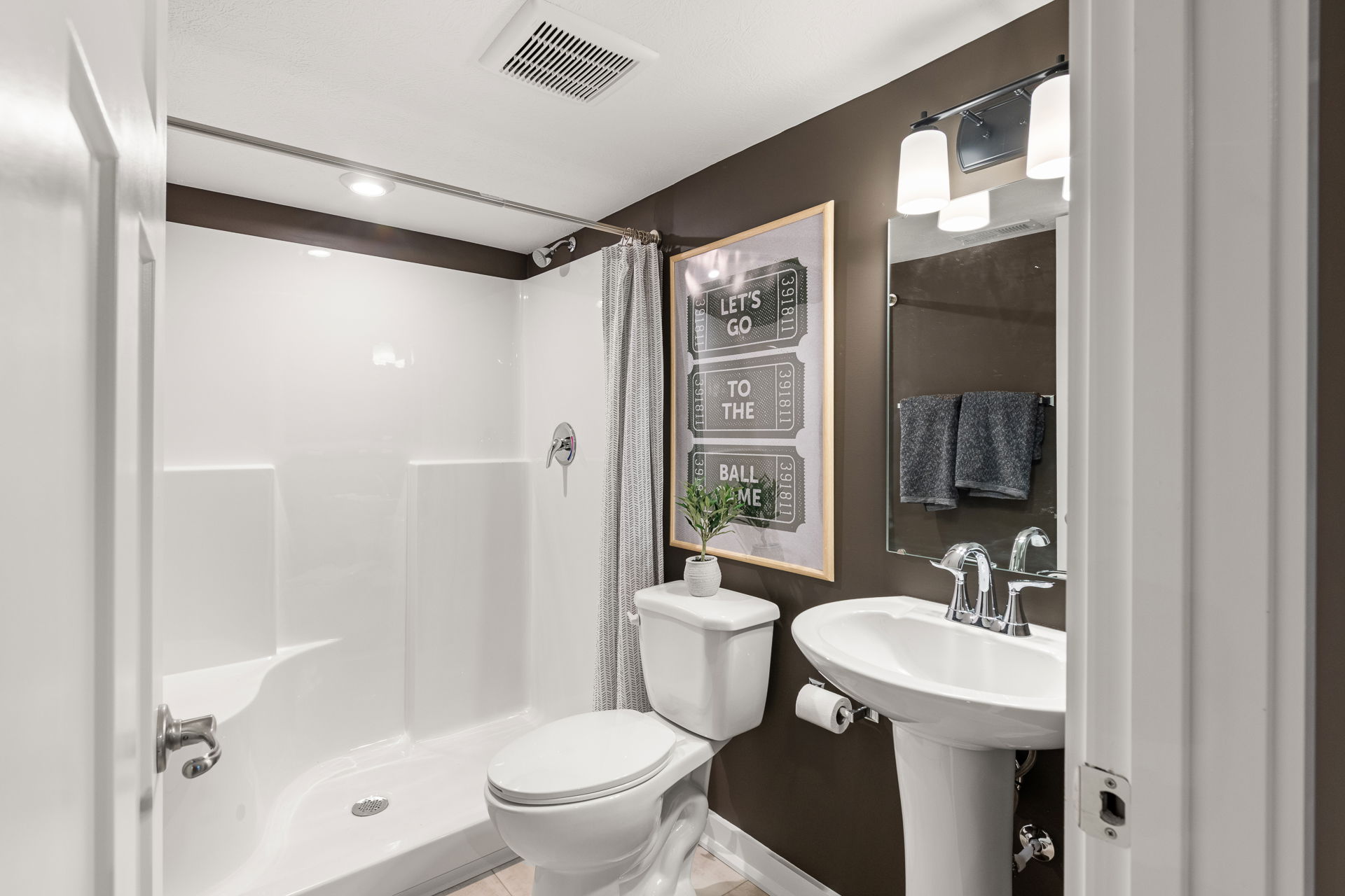 Modern bathroom with a walk-in shower, pedestal sink, and framed wall art featuring a game theme.