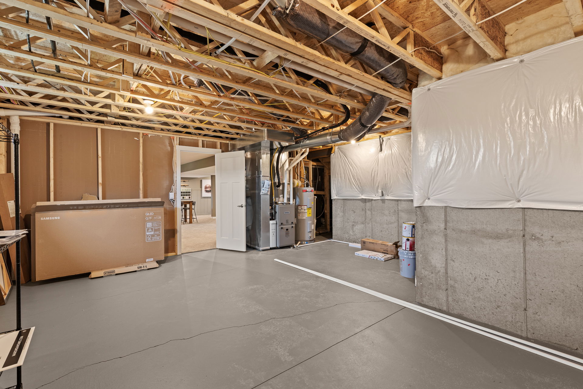Unfinished basement with exposed wooden beams, HVAC system, and a cardboard box leaning against the wall.