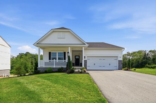 Single-story house with a porch, front lawn, and driveway under a clear blue sky.