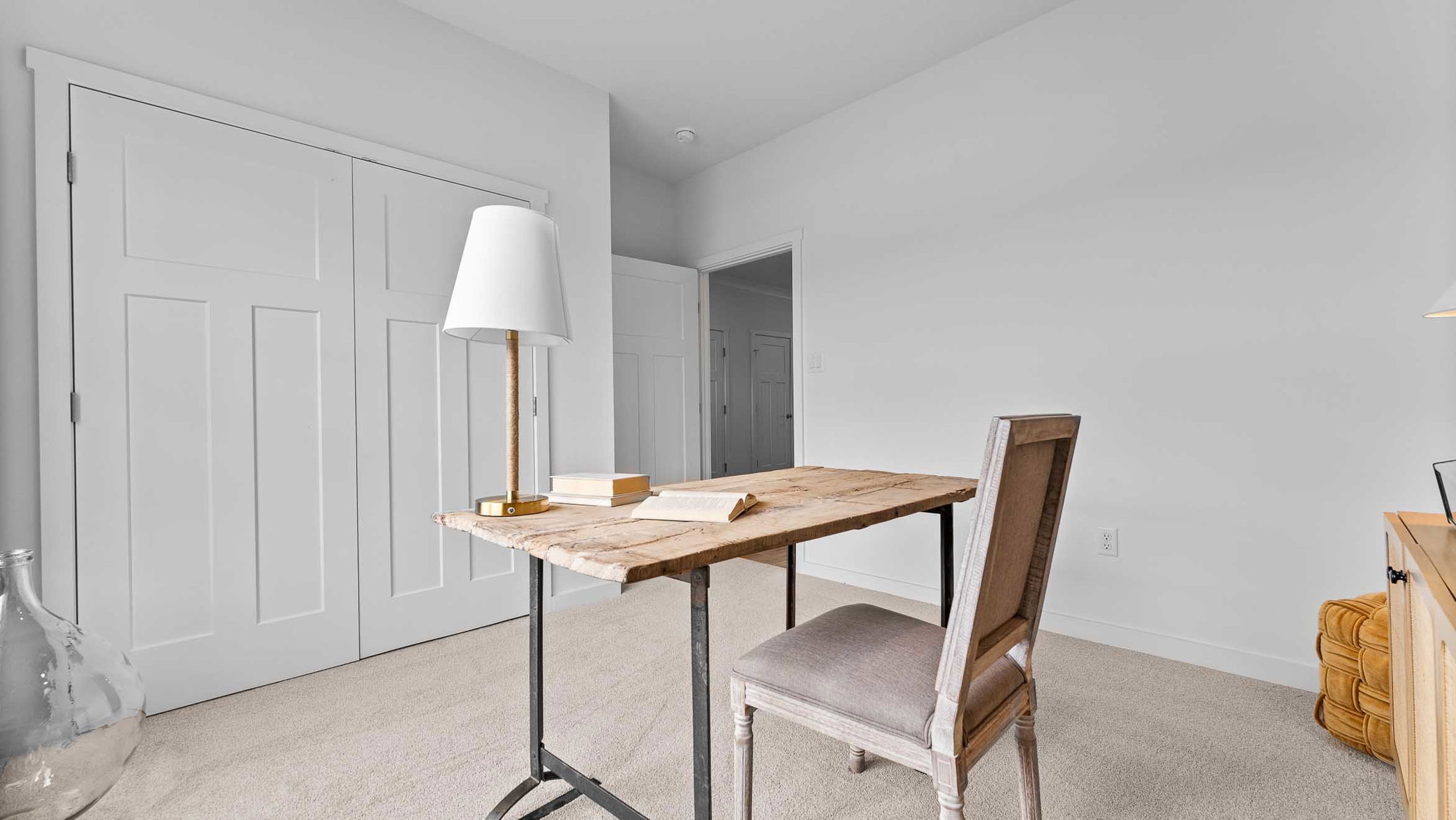 Minimalist home office with a rustic wooden desk, chair, and lamp against a light gray wall.