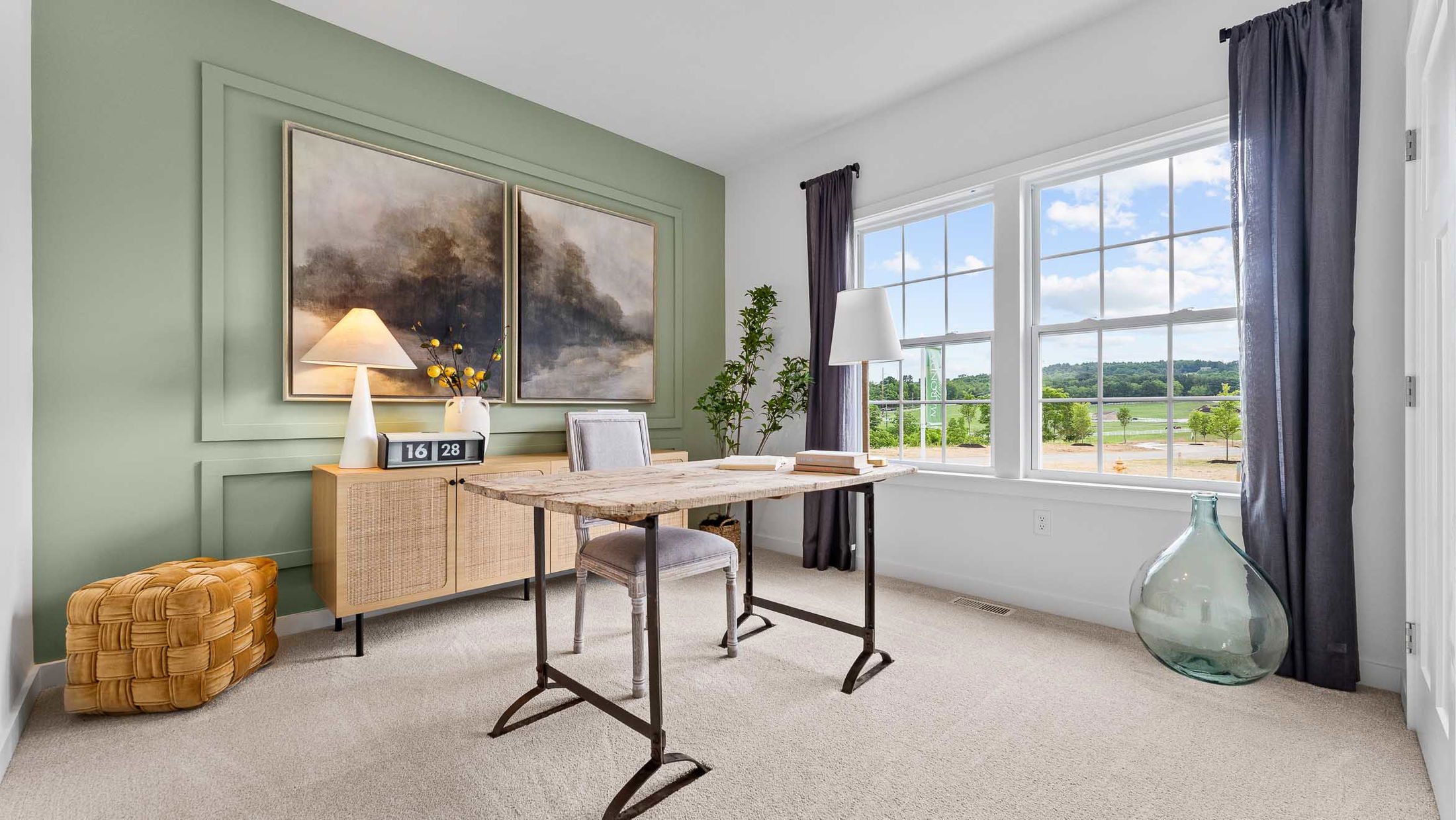Bright and spacious home office with a large window, rustic desk, modern art, and stylish decor overlooking a scenic landscape.
