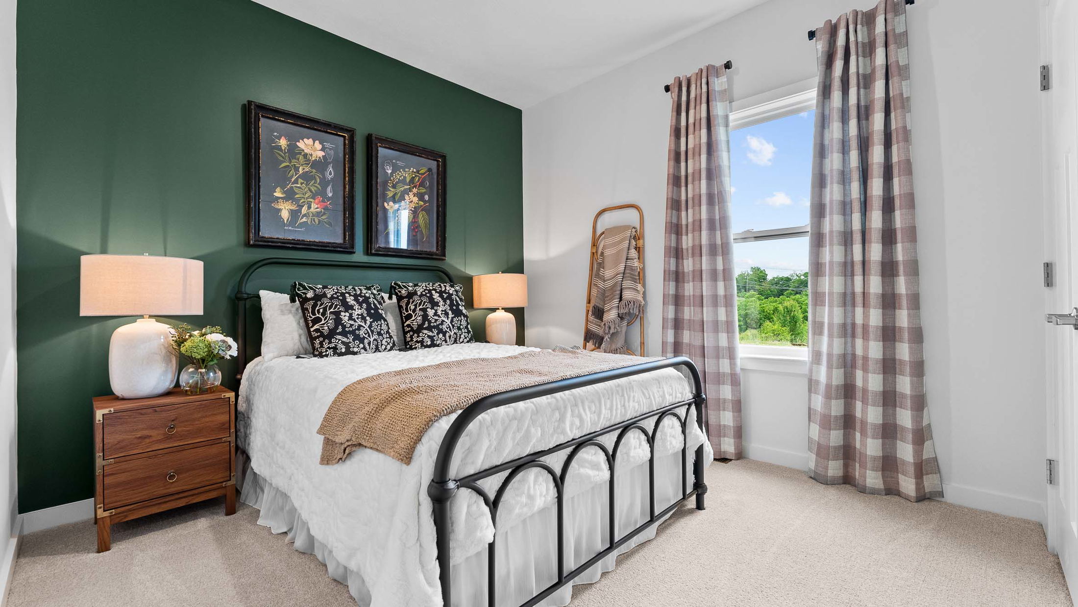 Modern bedroom with a black metal bedframe, green accent wall, floral artwork, and large window with plaid curtains.