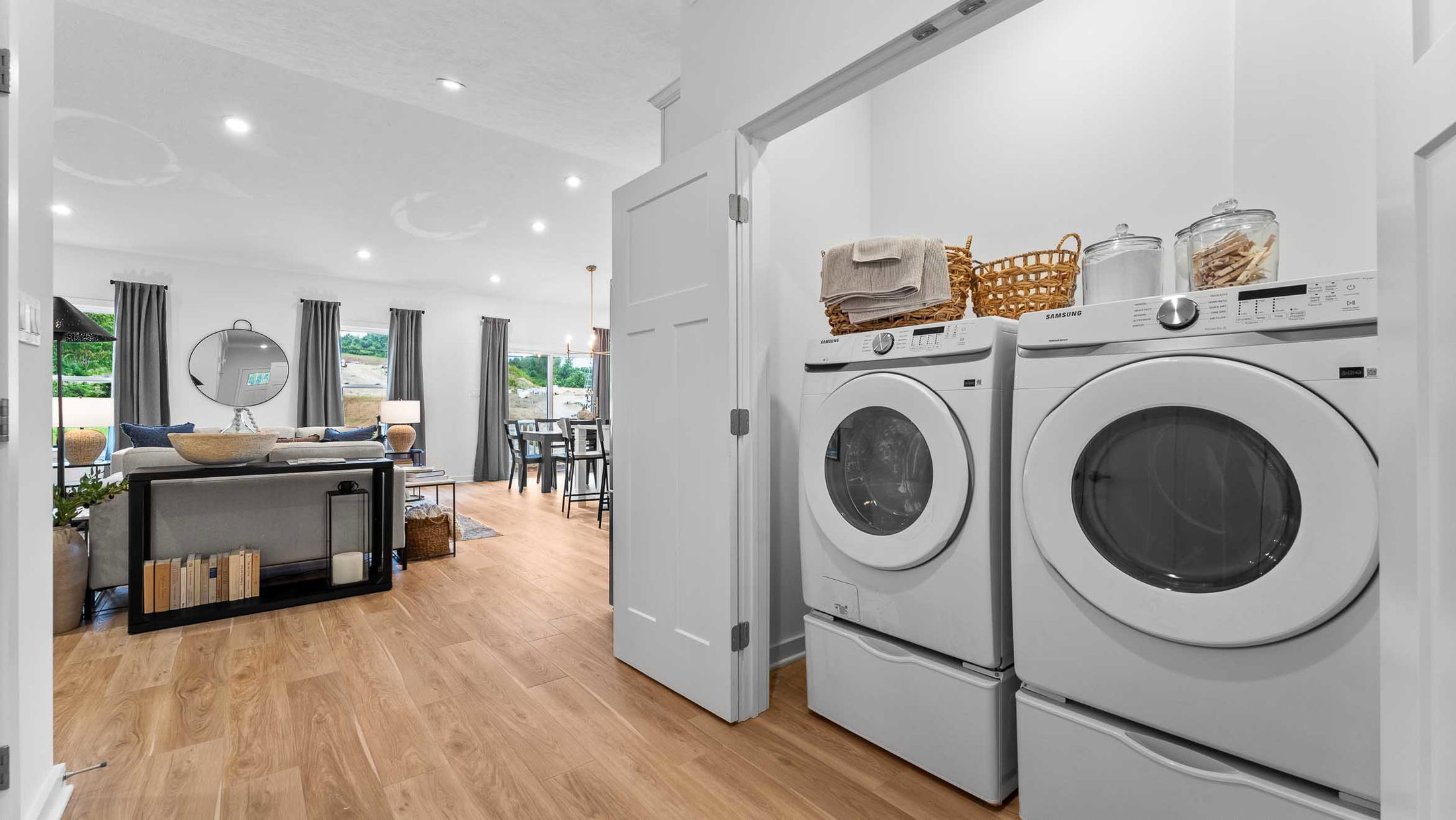 Stylish modern living room with hardwood floors, adjacent laundry area featuring Samsung washer and dryer, and elegant open floor plan.