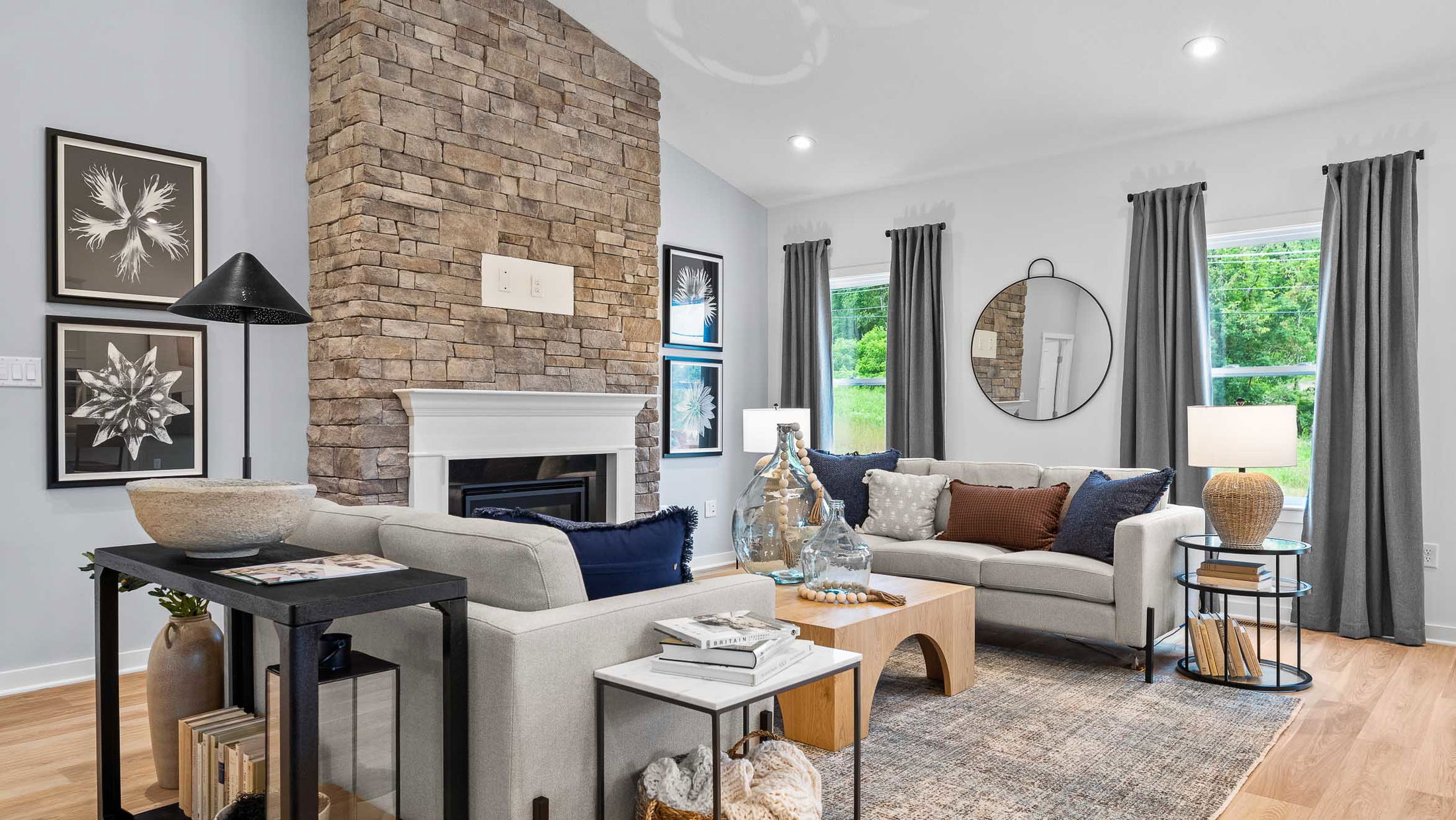 Modern living room with stone fireplace, gray sofas, and stylish decor elements including a round mirror and framed art.