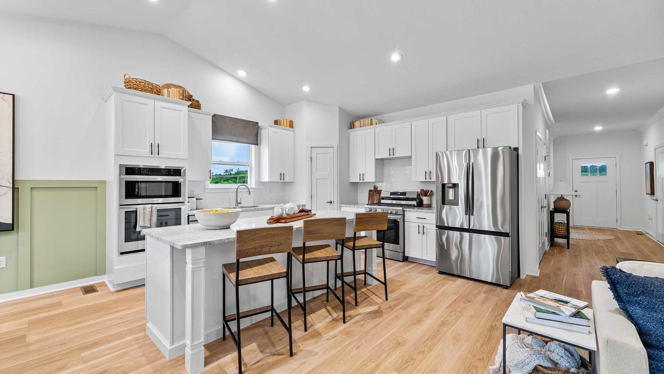 Modern kitchen interior with white cabinets, stainless steel appliances, and a central island with wooden barstools.